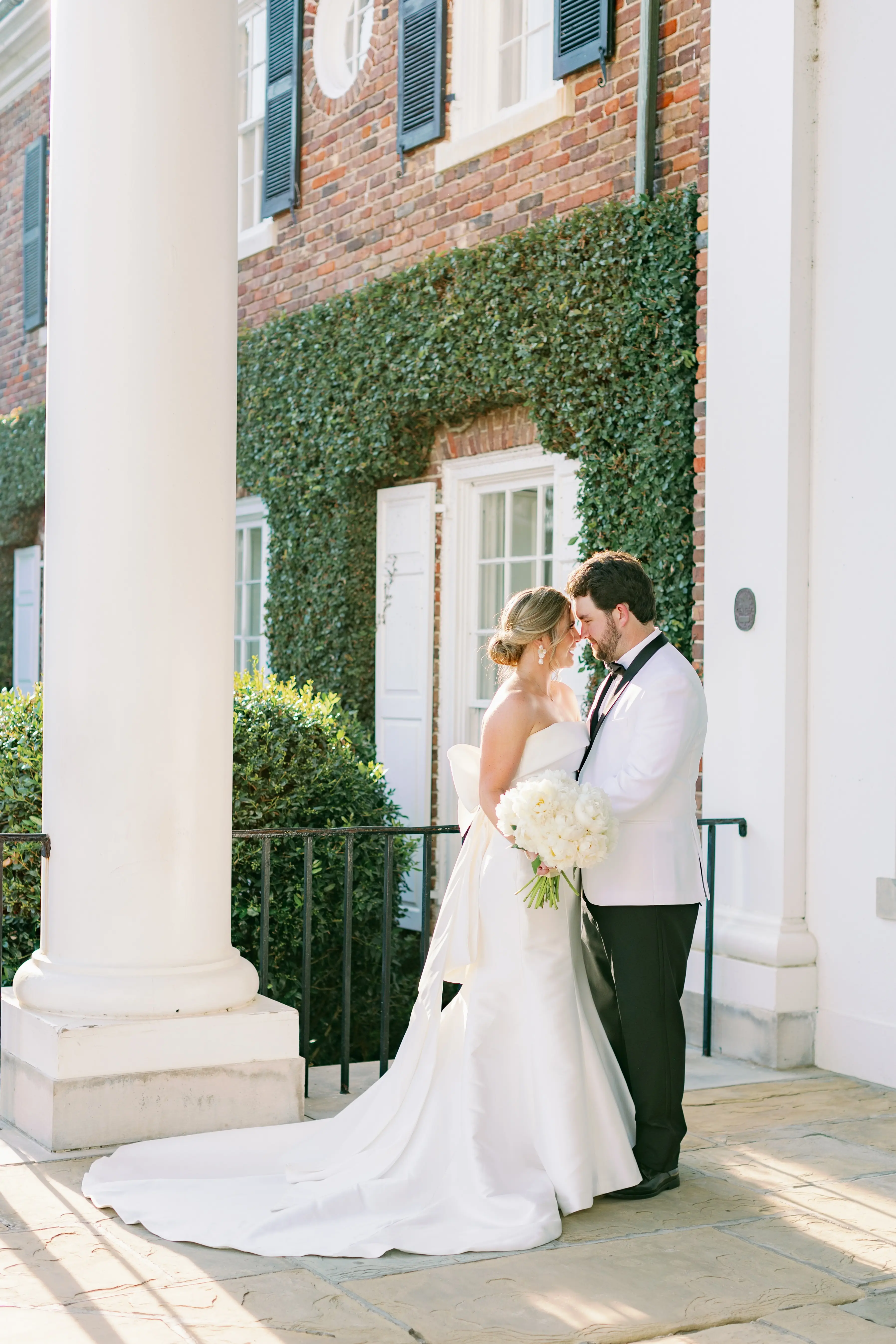 Bride with groom wearing strapless elegant mermaid wedding dress outdoors holding flower bouquet.