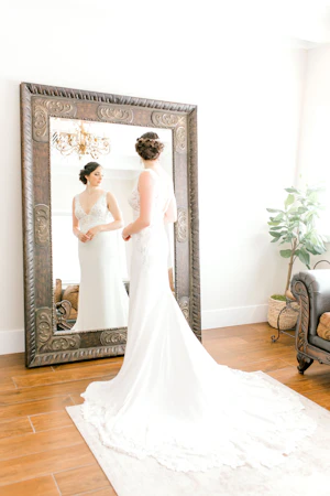 Bride looking into large mirror wearing wedding dress called Aidan.