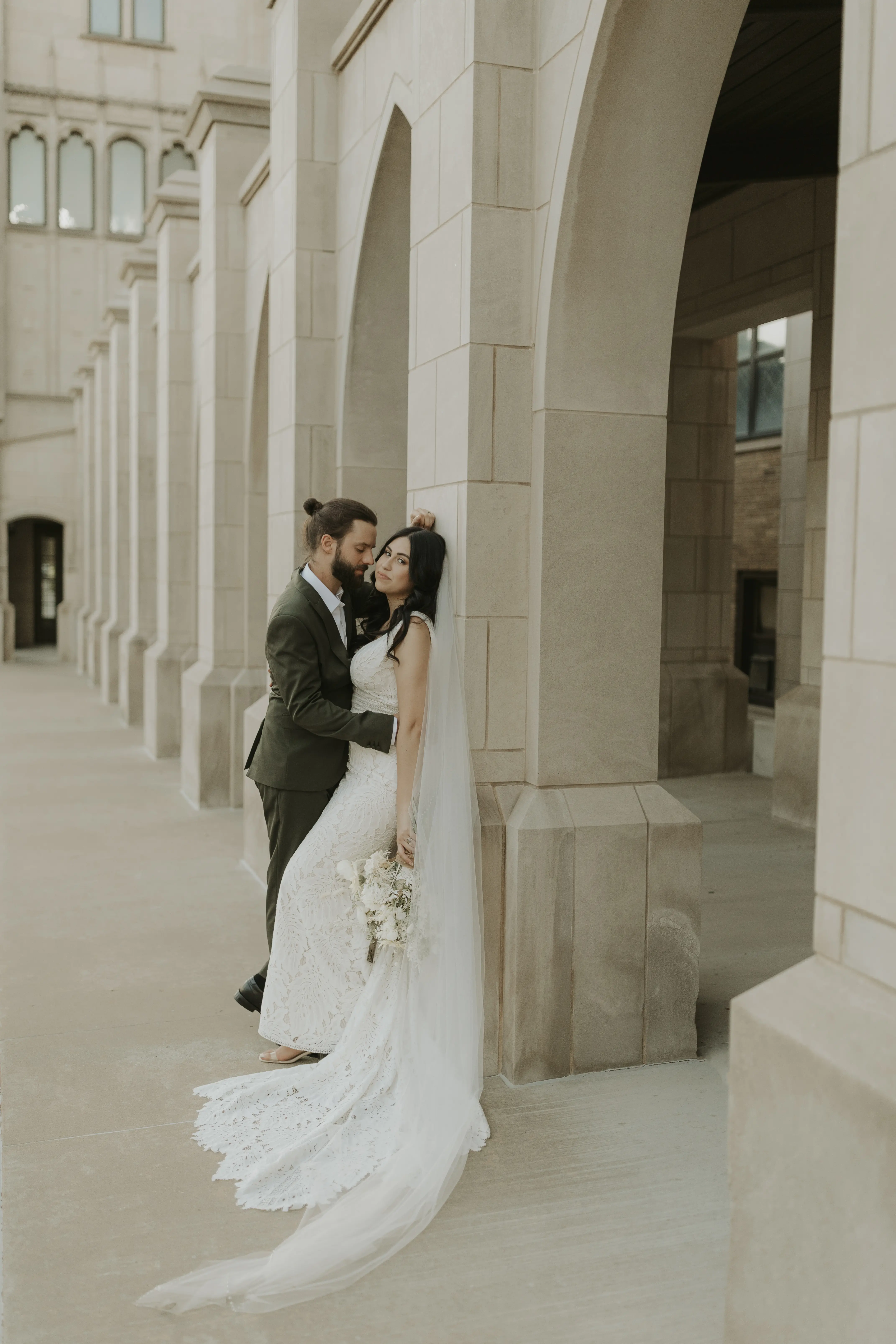 Bride against old building wall with groom hugging her.