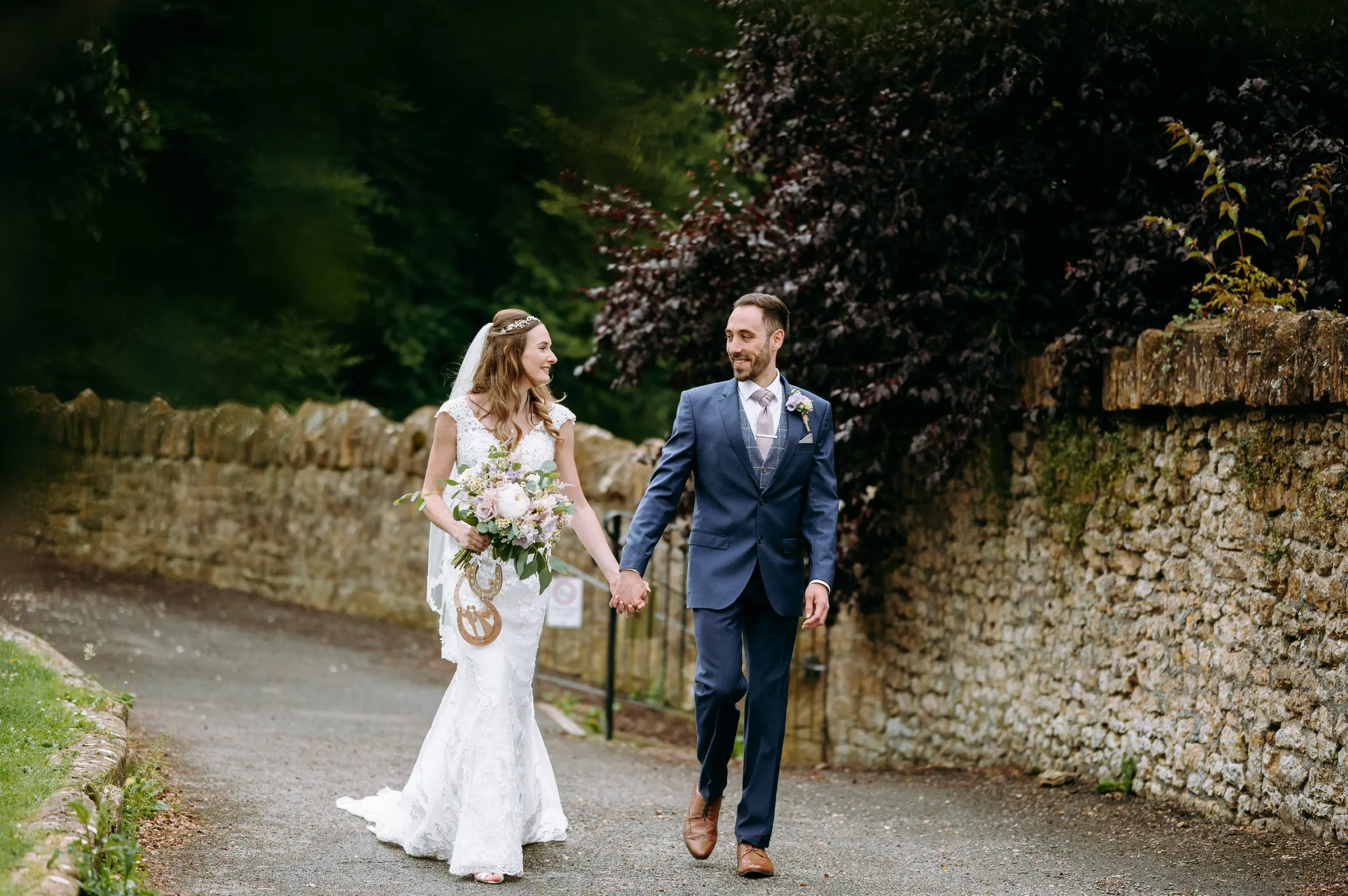 Newlyweds walking on a path looking at each other hand in hand.