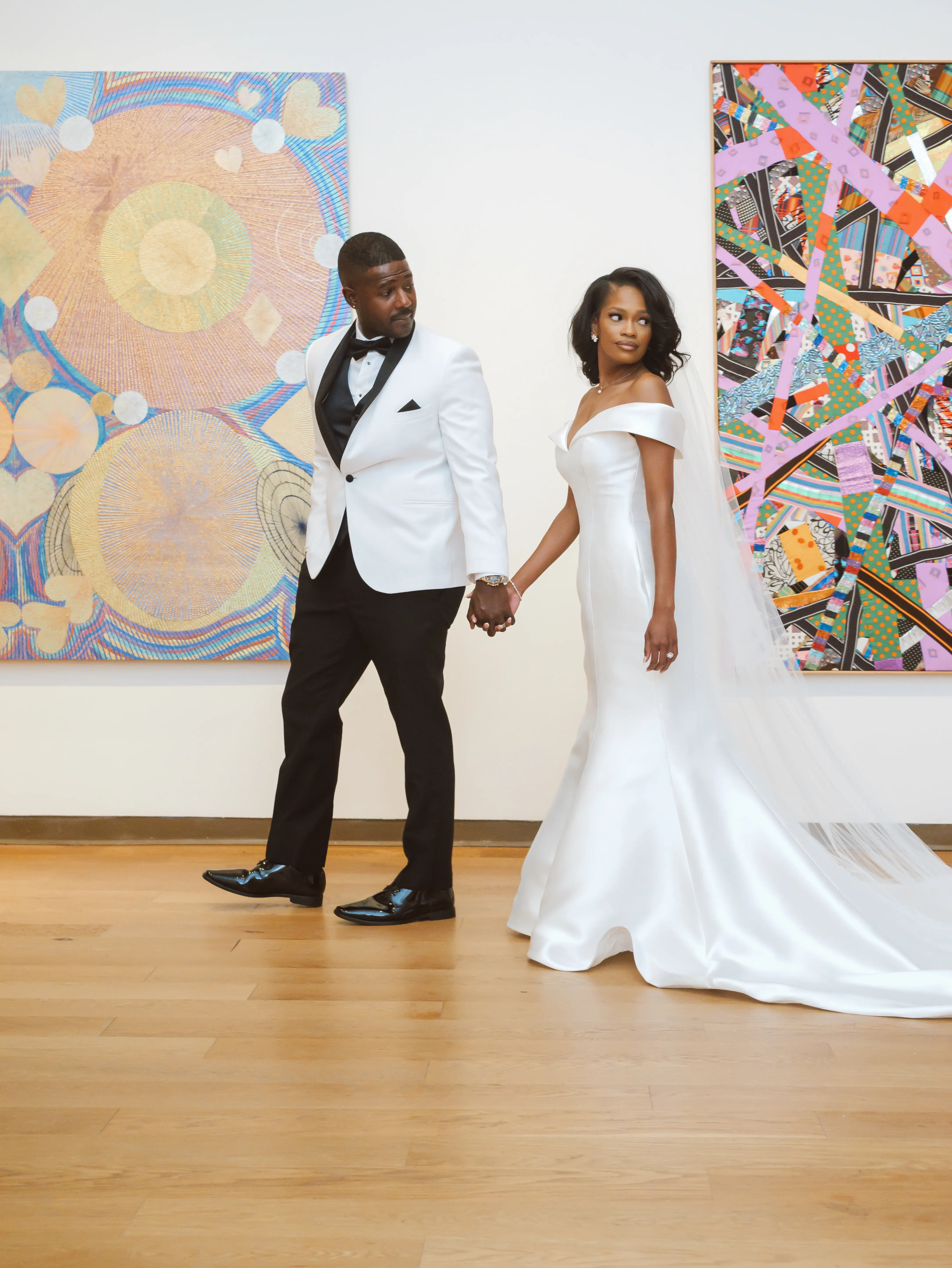 Bride Wearing Simple Mermaid Wedding Dress Called Josie By Rebecca Ingram Holding Hands With Groom In An Art Exhibit