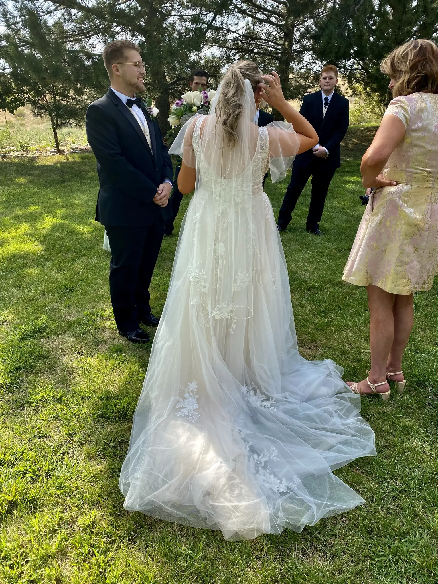 Bride wearing romantic lace A-line dress called Raelynn by Rebecca Ingram with wedding guests
