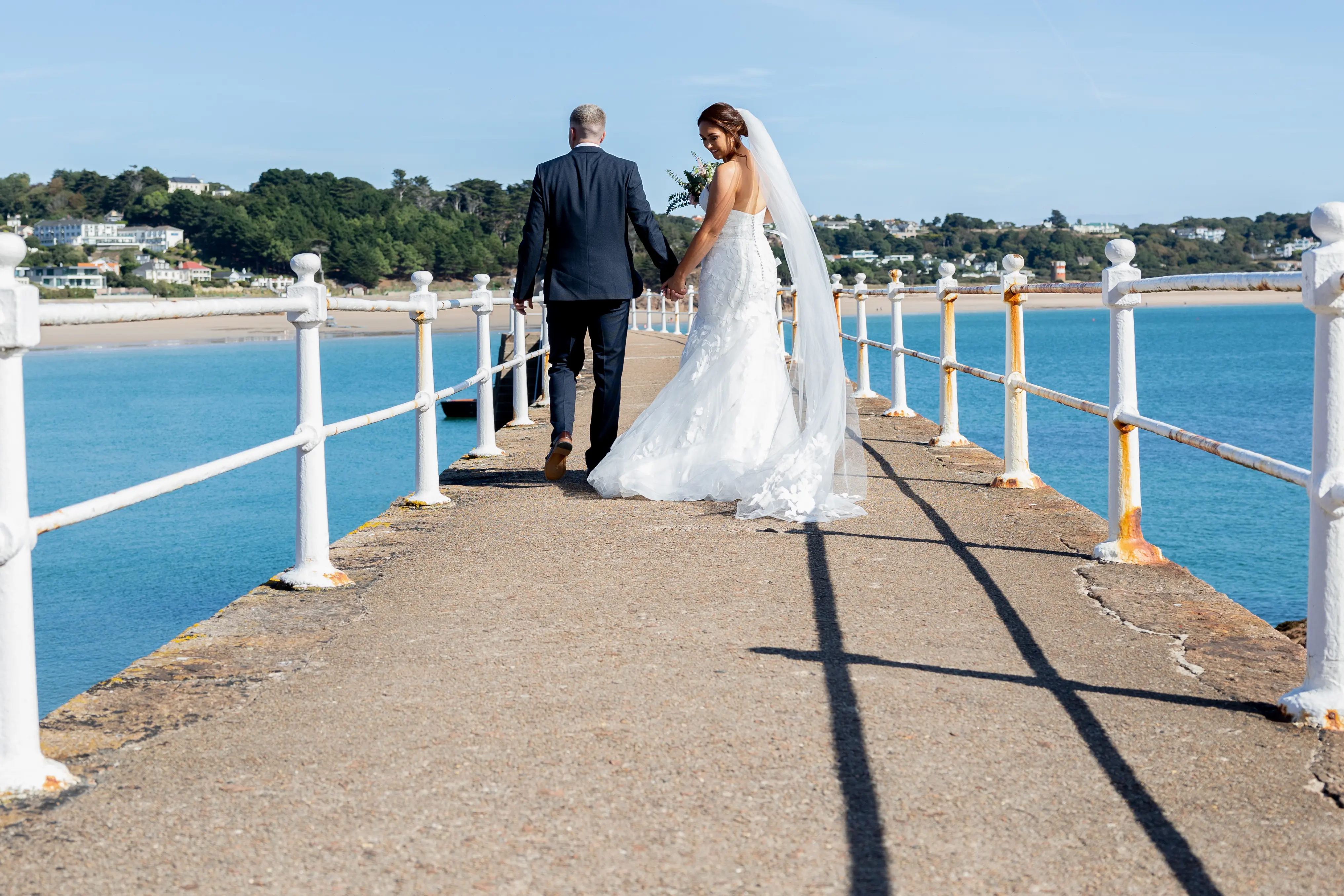 Bride Wearing Lace Mermaid Wedding Dress Called Hattie By Rebecca Ingram Walking With Groom On A Pier
