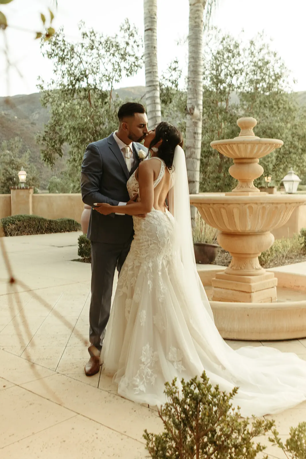 Bride and groom kissing next to a large fountain.