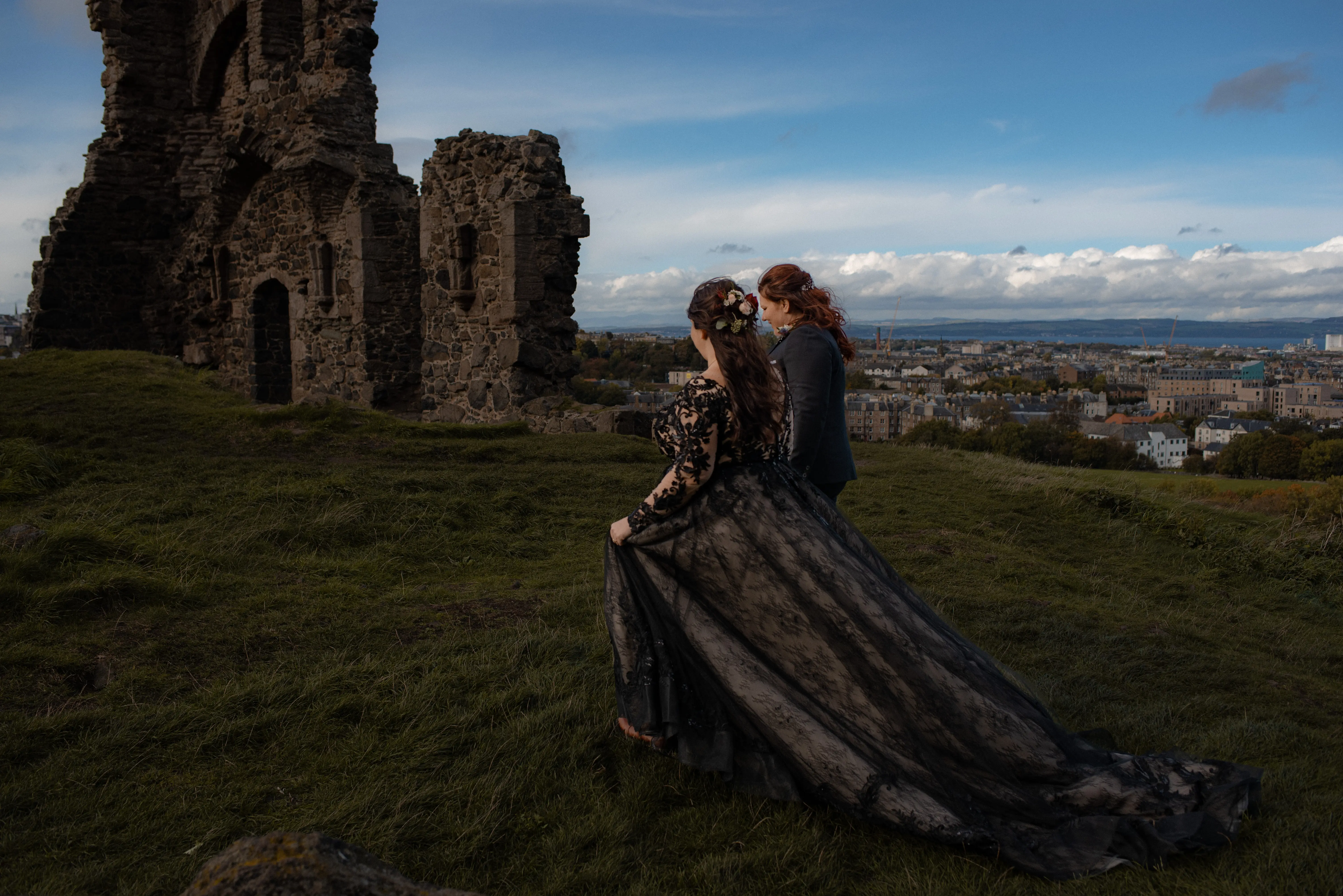 Bride Wearing Black A-Line Wedding Dress Called Zander By Sottero And Midgley Walking With Bride Near Castle Ruins