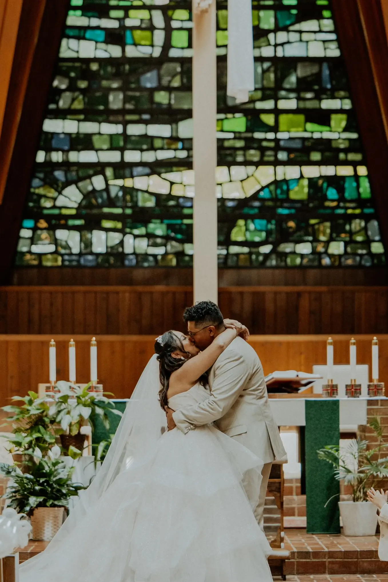 Bride Wearing Tiered Princess Skirt Wedding Dress Called Yasmin By Maggie Sottero Kissing Groom Under Stained Glass Window
