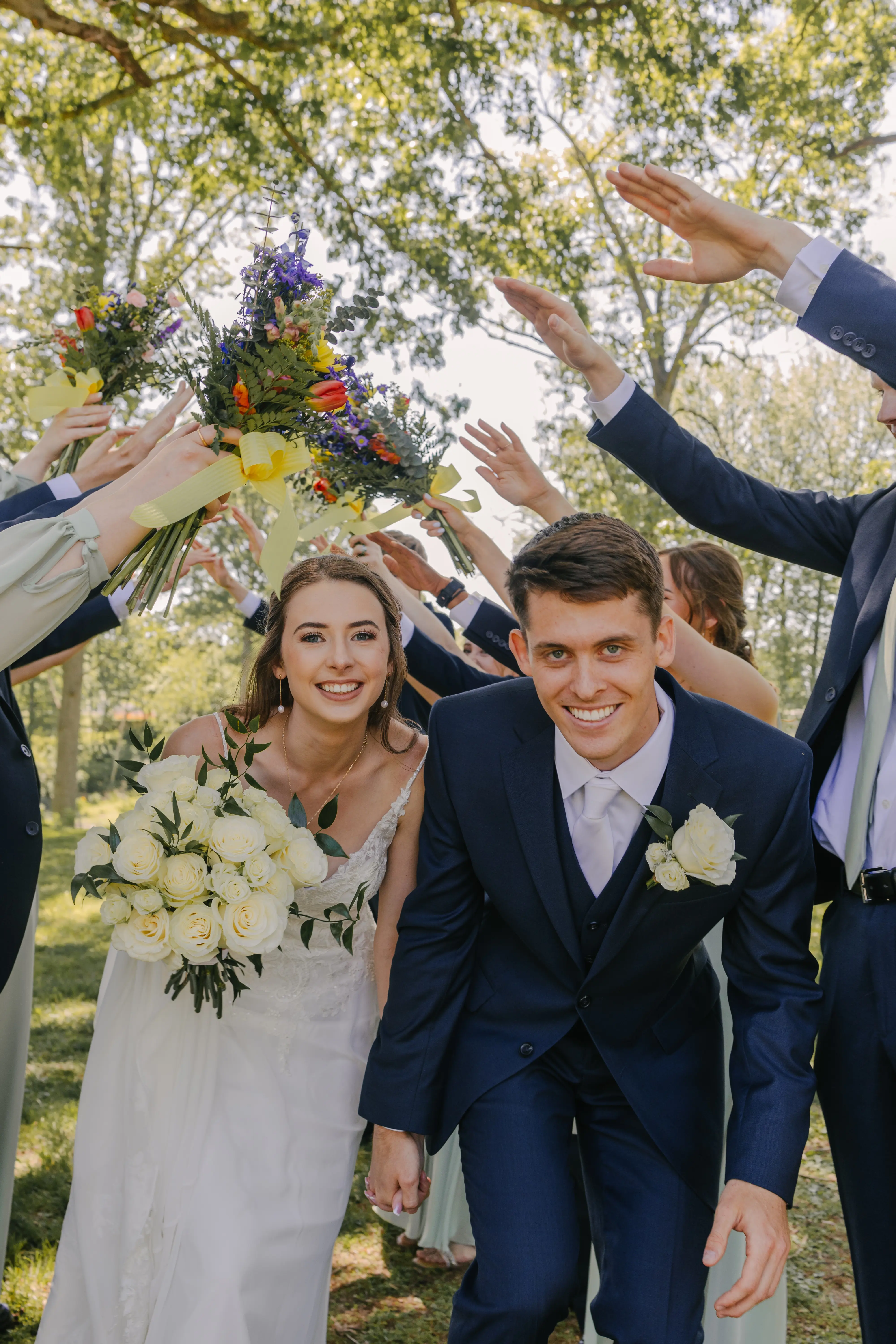 Bride wearing Charlotte by Rebecca Ingram going under a bridge of bridesmaids and groomsmen