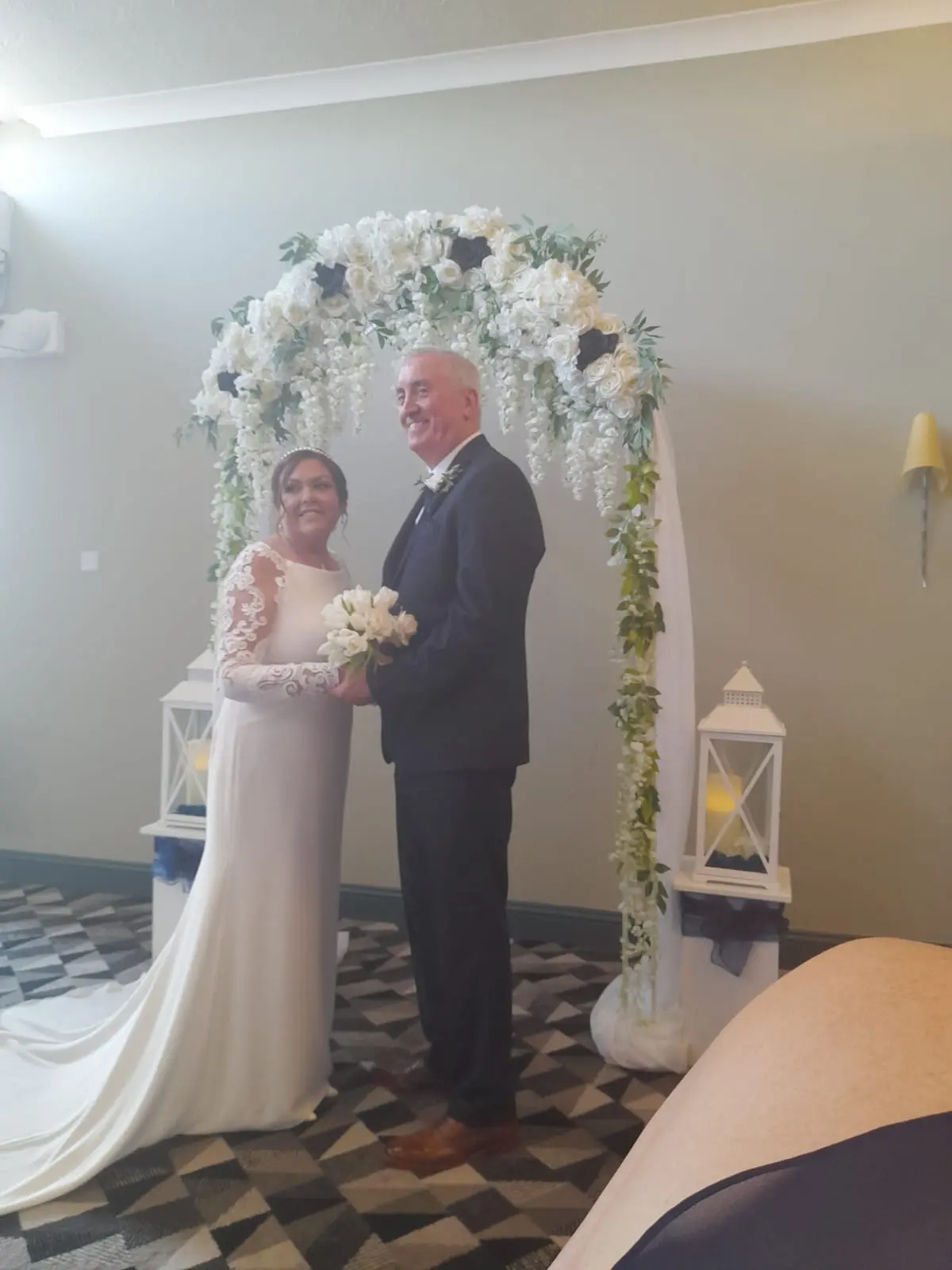 Bride in Crepe Long Sleeve Lace Sheath Wedding Dress named Bethany by Rebecca Ingram Bride with Groom under flowers