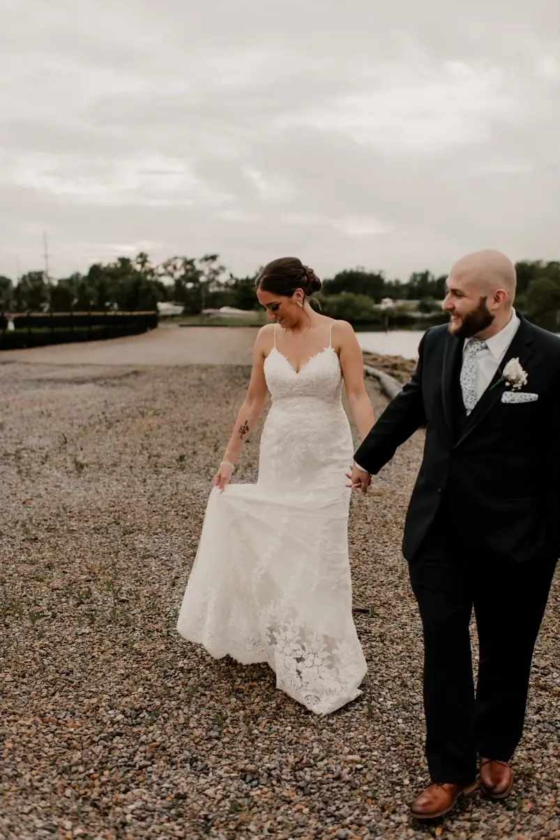 Groom smiling holding brides hand as she looks down admiring her lovely lace wedding dress..