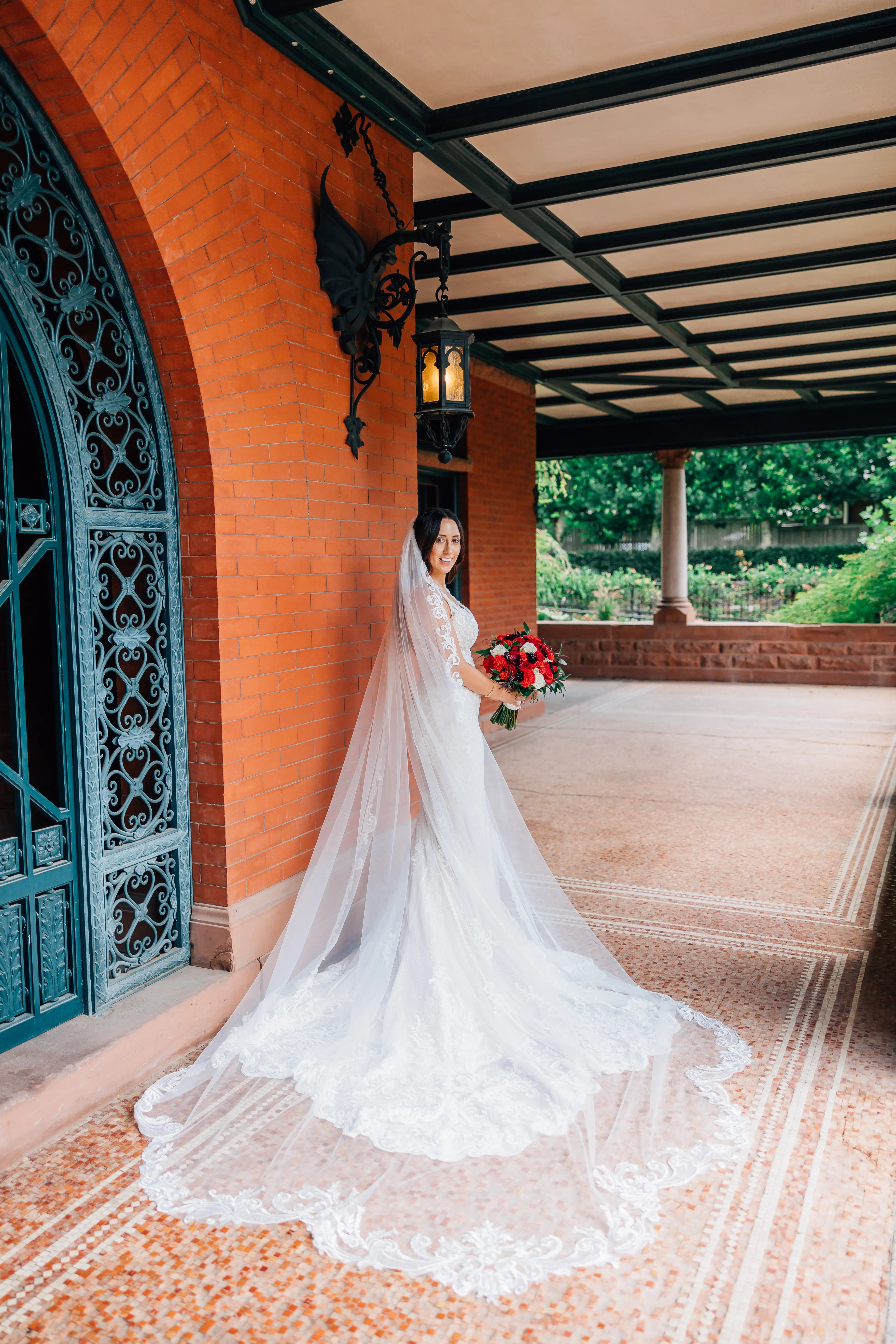 Real Bride Wearing A Fitted White Wedding Dress Named Veronique by Maggie Sottero With Long Veil And Red Roses