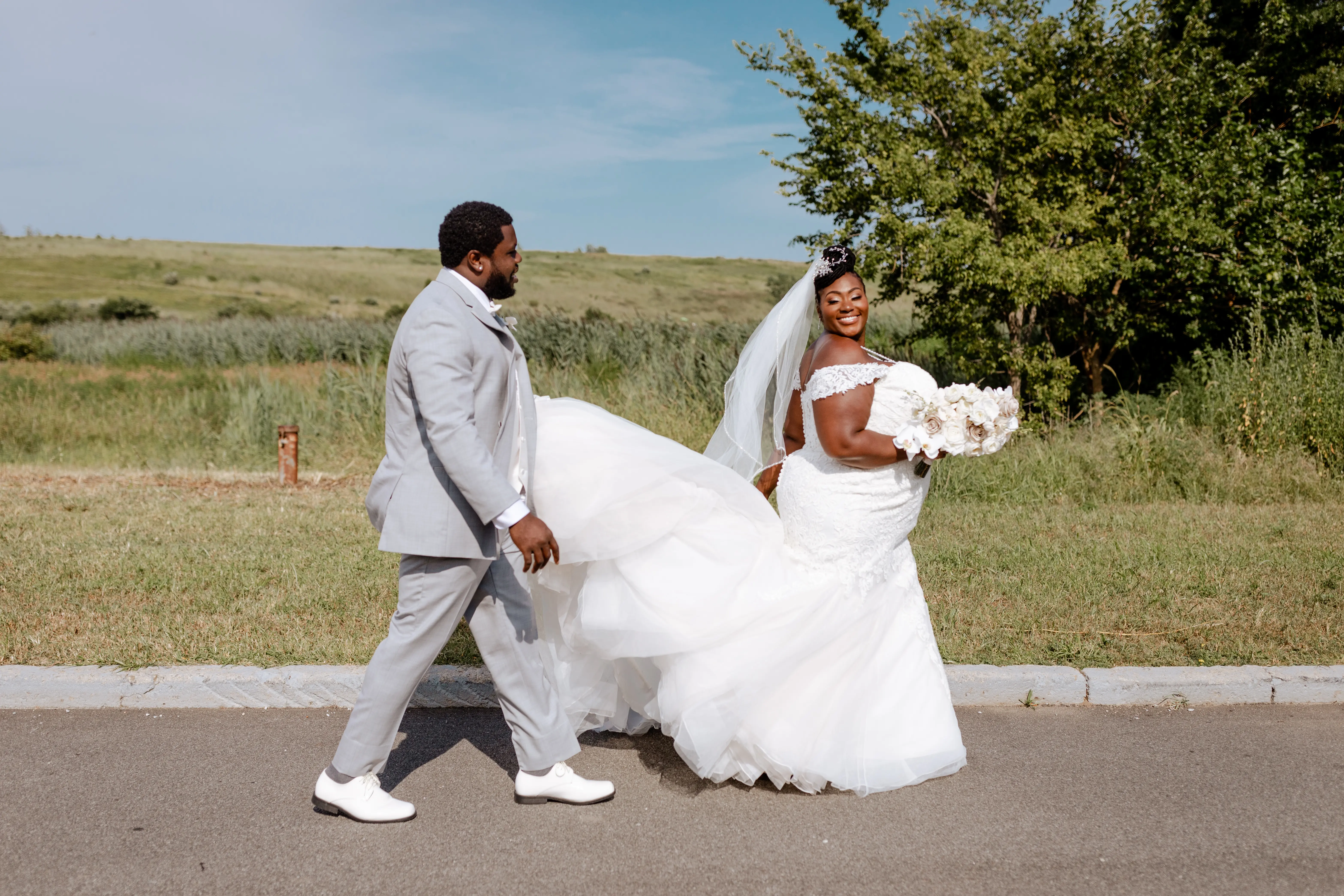 Groom holding his bride's train of wedding dress called Alistaire Lynette.