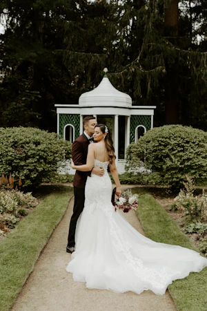 Bride with groom wearing lace fit-and-flare wedding dress holding bridal bouquet outdoors.