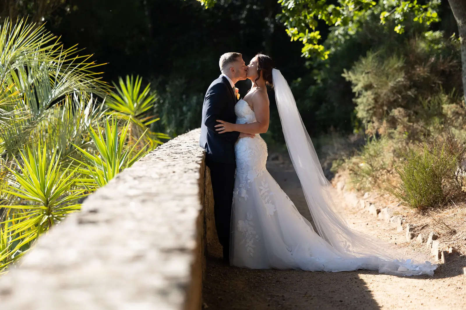 Bride Wearing Lace Mermaid Wedding Dress Called Hattie By Rebecca Ingram Kissing Groom In A Garden