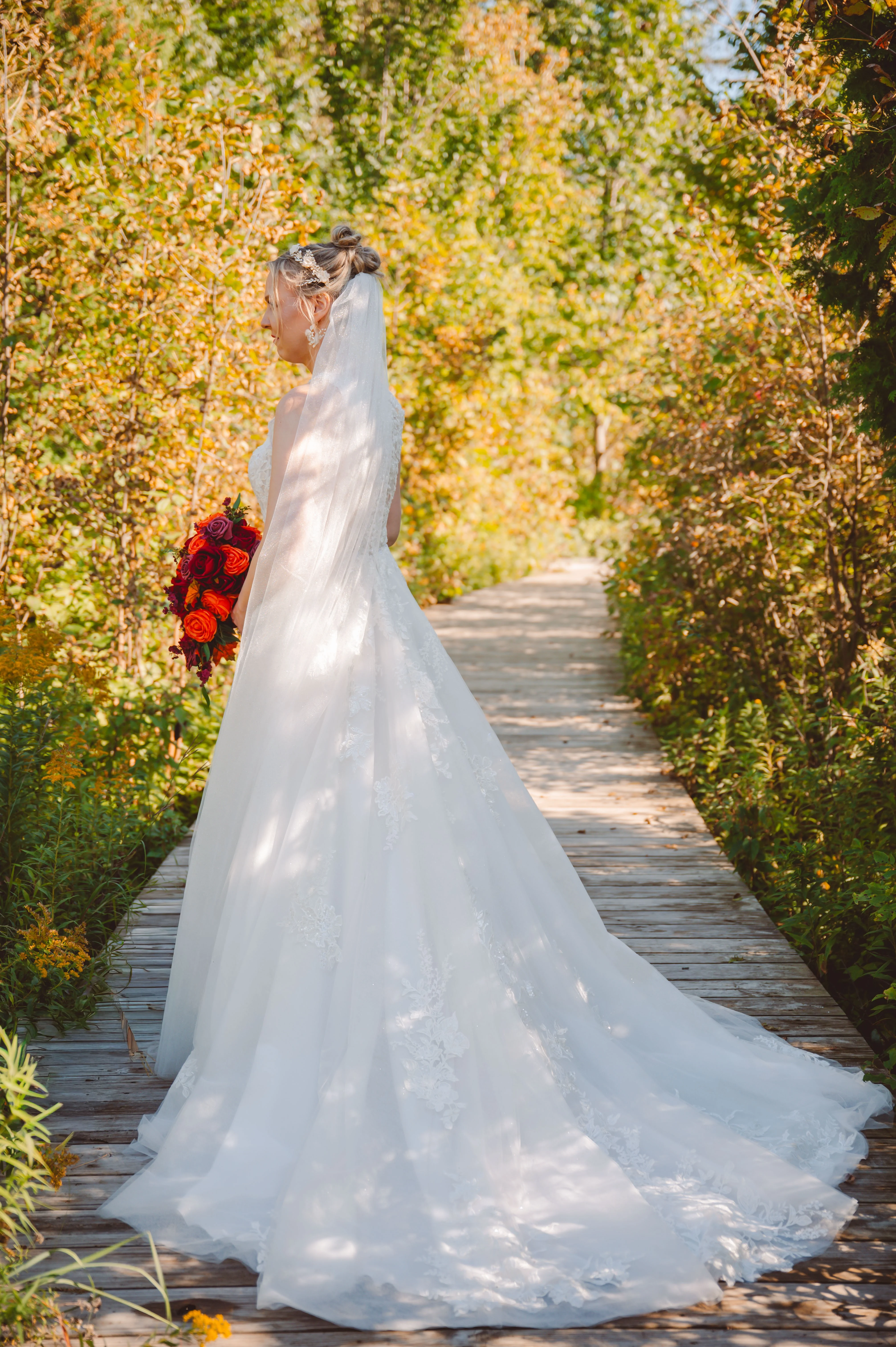 Bride wearing Lace Aline Wedding Dress Called Rickie By Rebecca Ingram On A Path Near Fall Trees