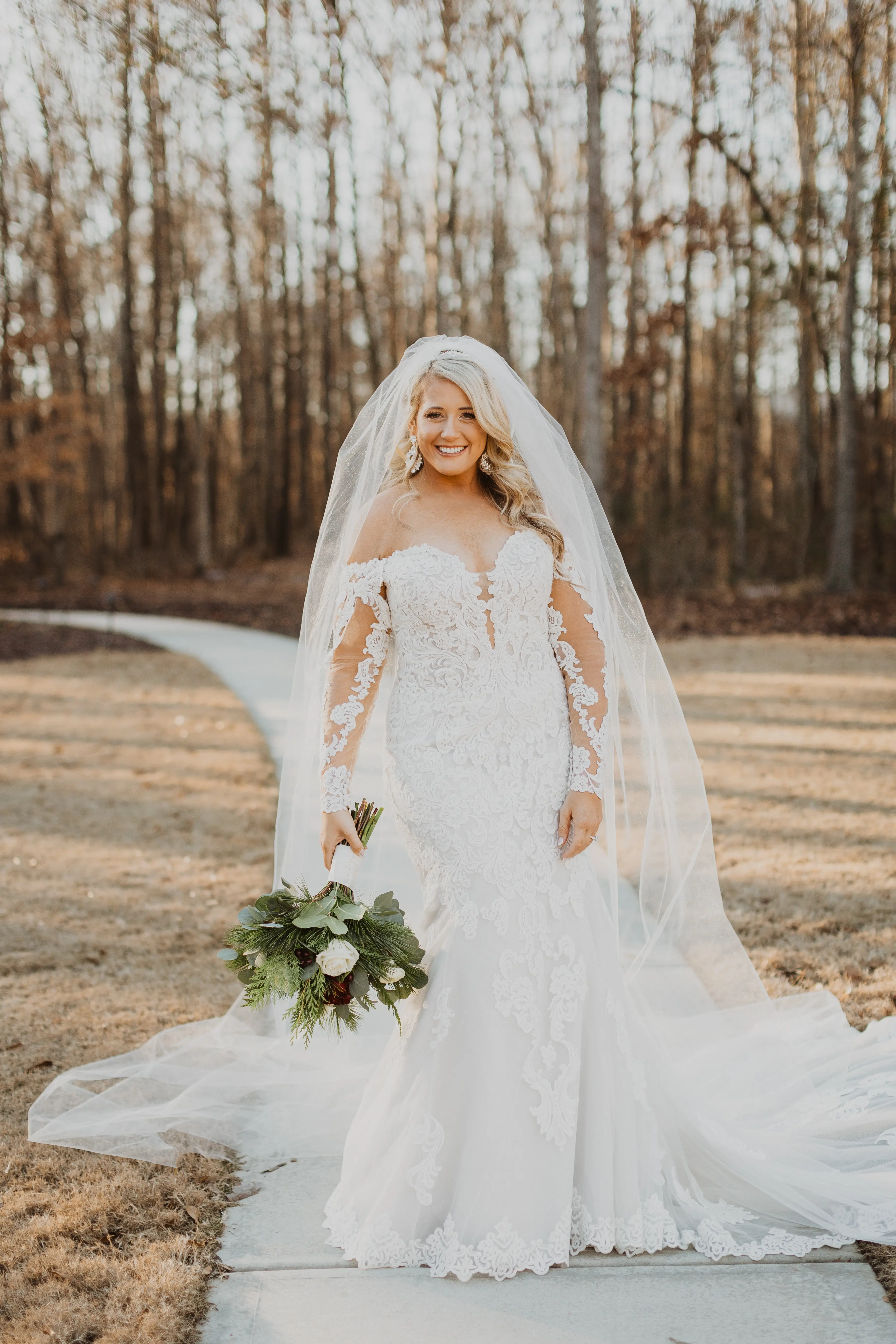 Bride In A Sparkly Lace Fit-And-Flare Wedding Dress Named Fiona By Maggie Sottero With A Long Veil And Flower Bouquet