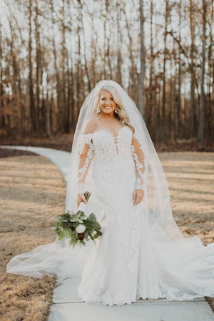 Bride In A Sparkly Lace Fit-And-Flare Wedding Dress Named Fiona By Maggie Sottero With A Long Veil And Flower Bouquet