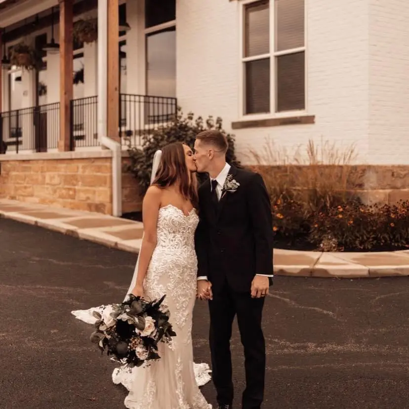 Bride with groom outdoors wearing strapless lace fit and flare wedding dress.