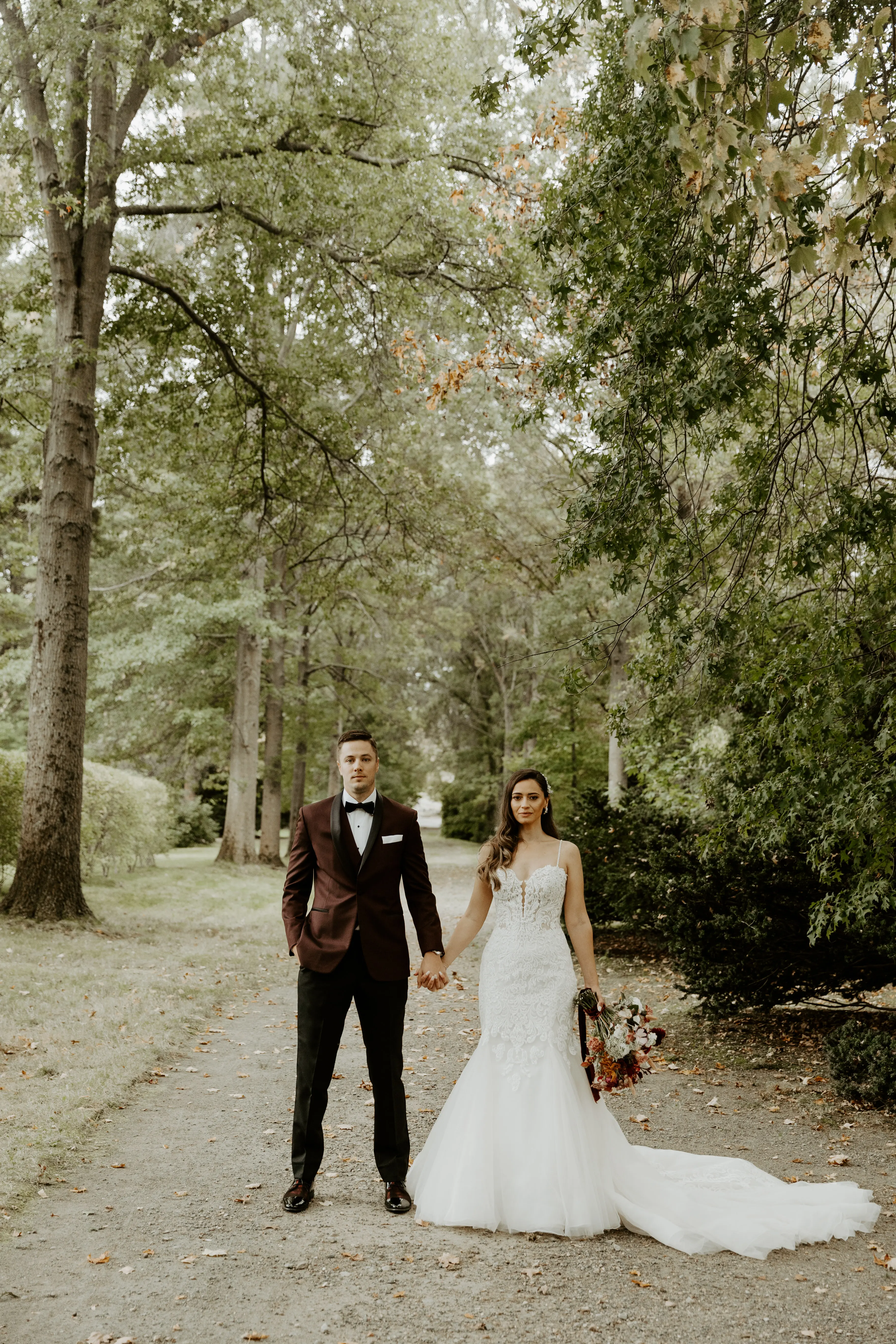 Bride with groom wearing lace fit-and-flare wedding dress holding bridal bouquet outdoors.