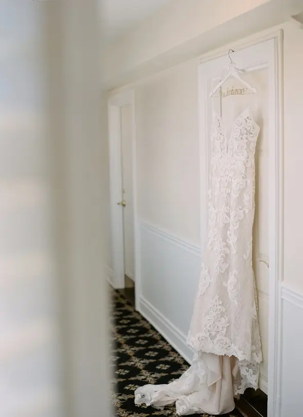 Detailed lace wedding dress called Tuscany Lynette hanging on door.