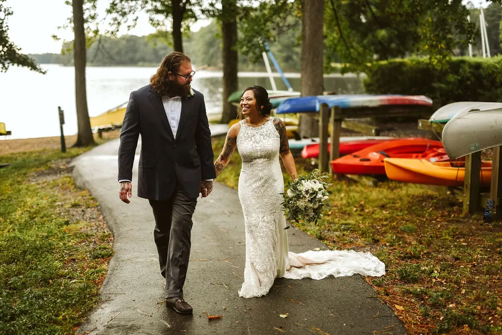 Bride Wearing Halter Lace Wedding Dress Called Kevyn By Sottero And Midgley Walking With Groom By A Lake