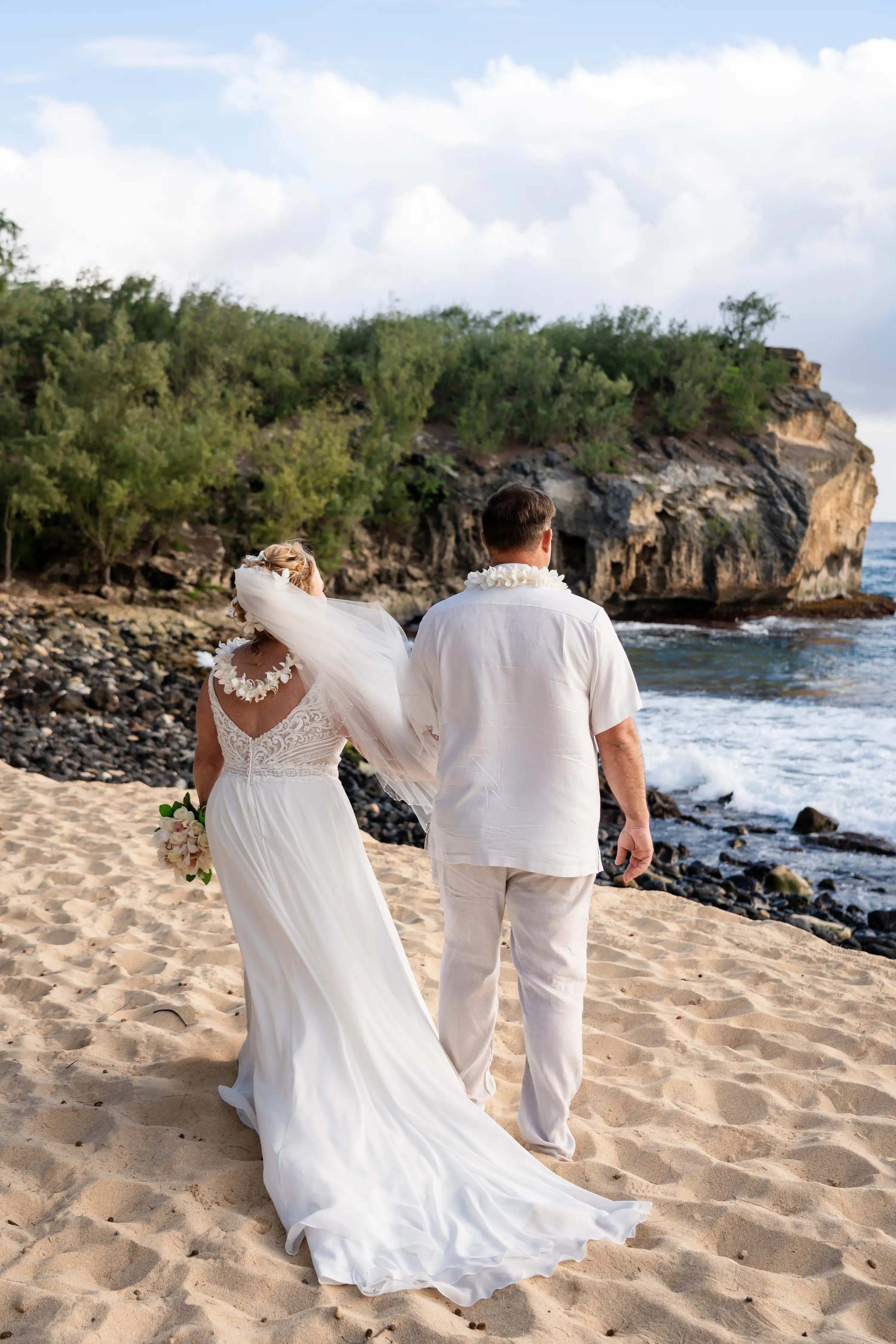 Bride wearing Lorraine wedding dress by Rebecca Ingram walking on the beach with her husband