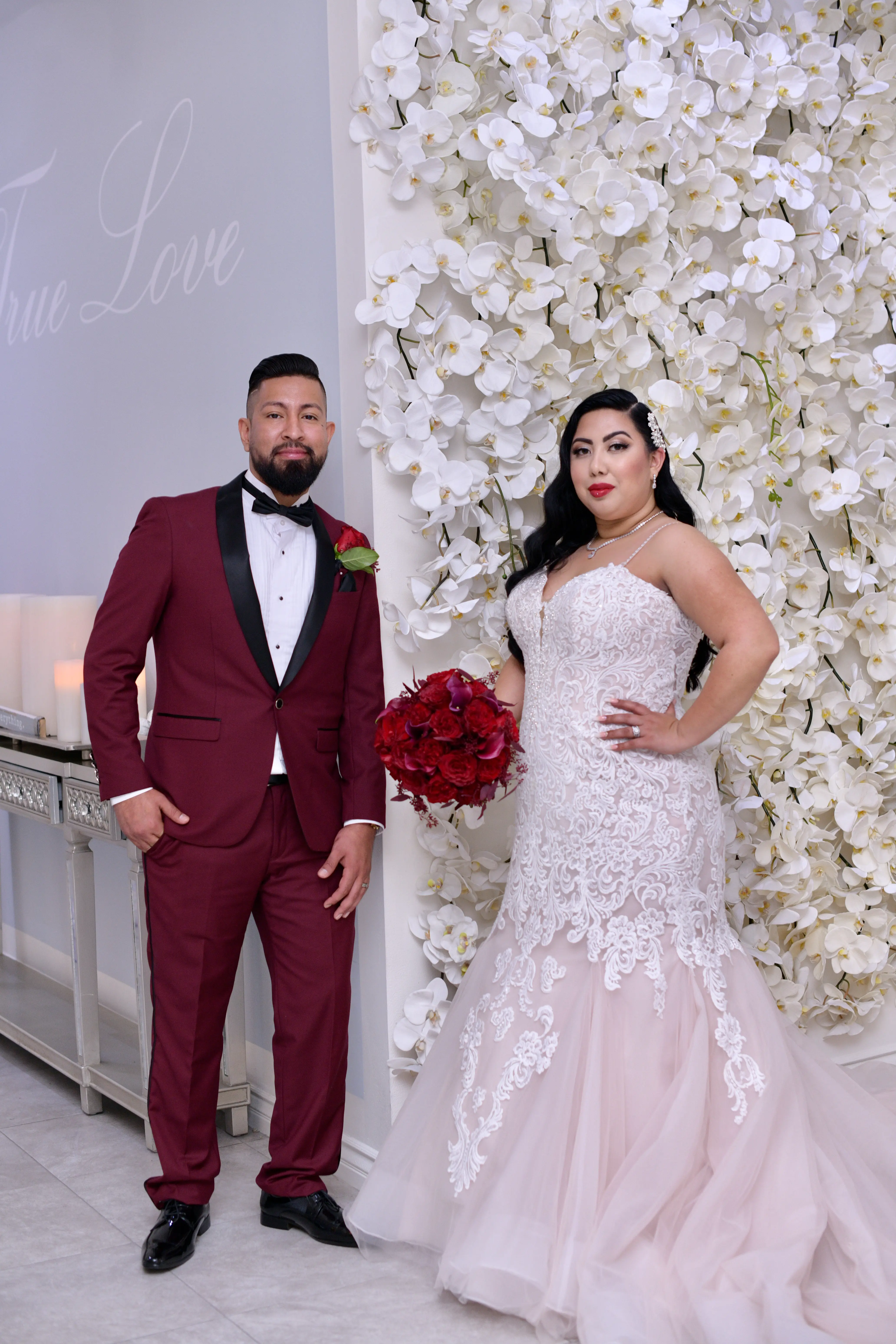 Groom wearing burgundy suit stood with bride wearing wedding dress called Alistaire Lynette.