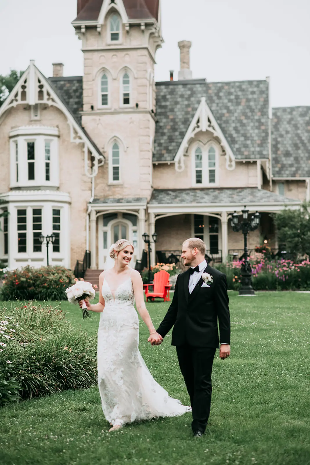 Newlyweds holding hands looking at each other in front of a beautiful stately home.