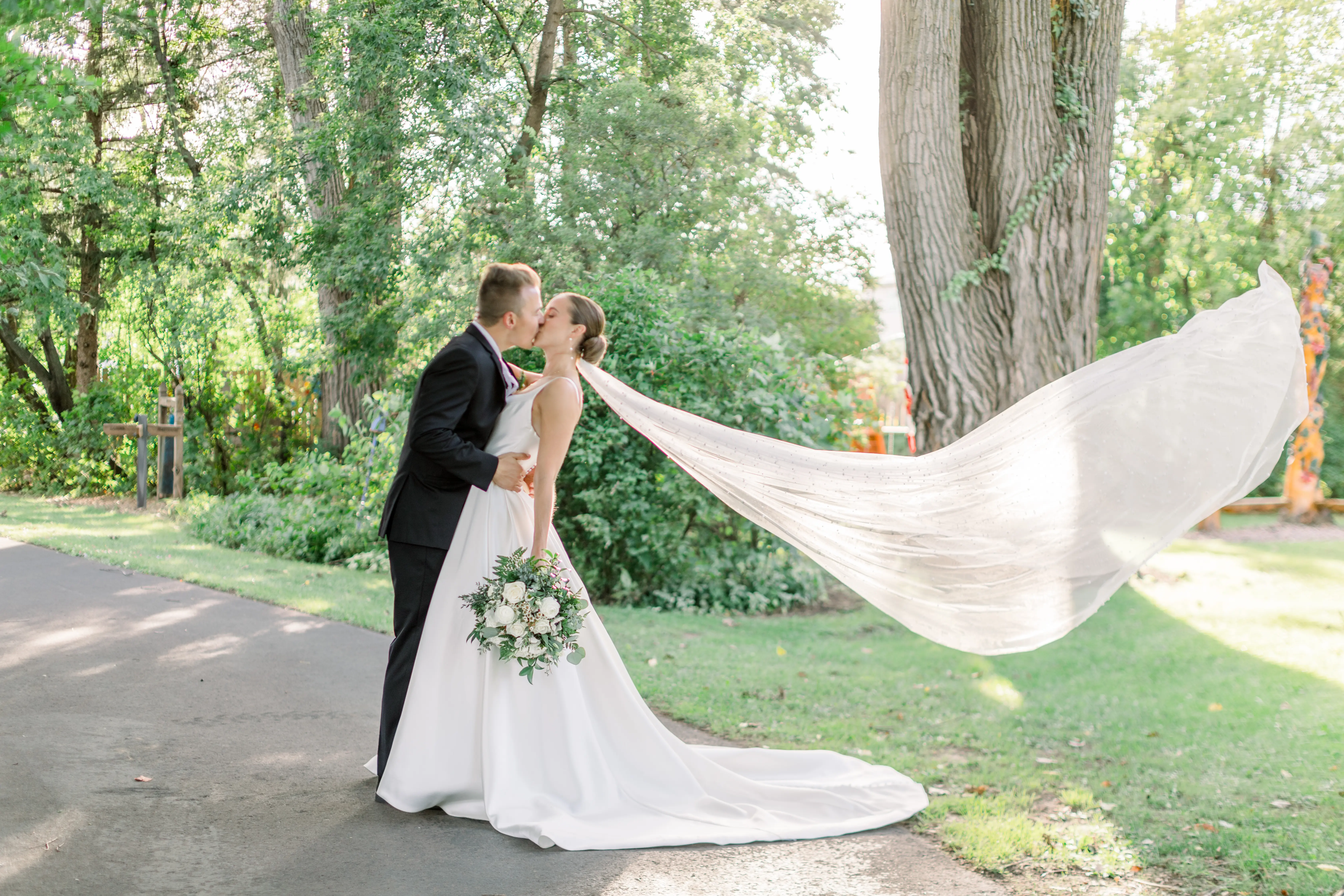 Bride Wearing Classic A-Line Wedding Dress Called Selena By Maggie Sottero Kissing Groom With Veil Blowing In The Wind