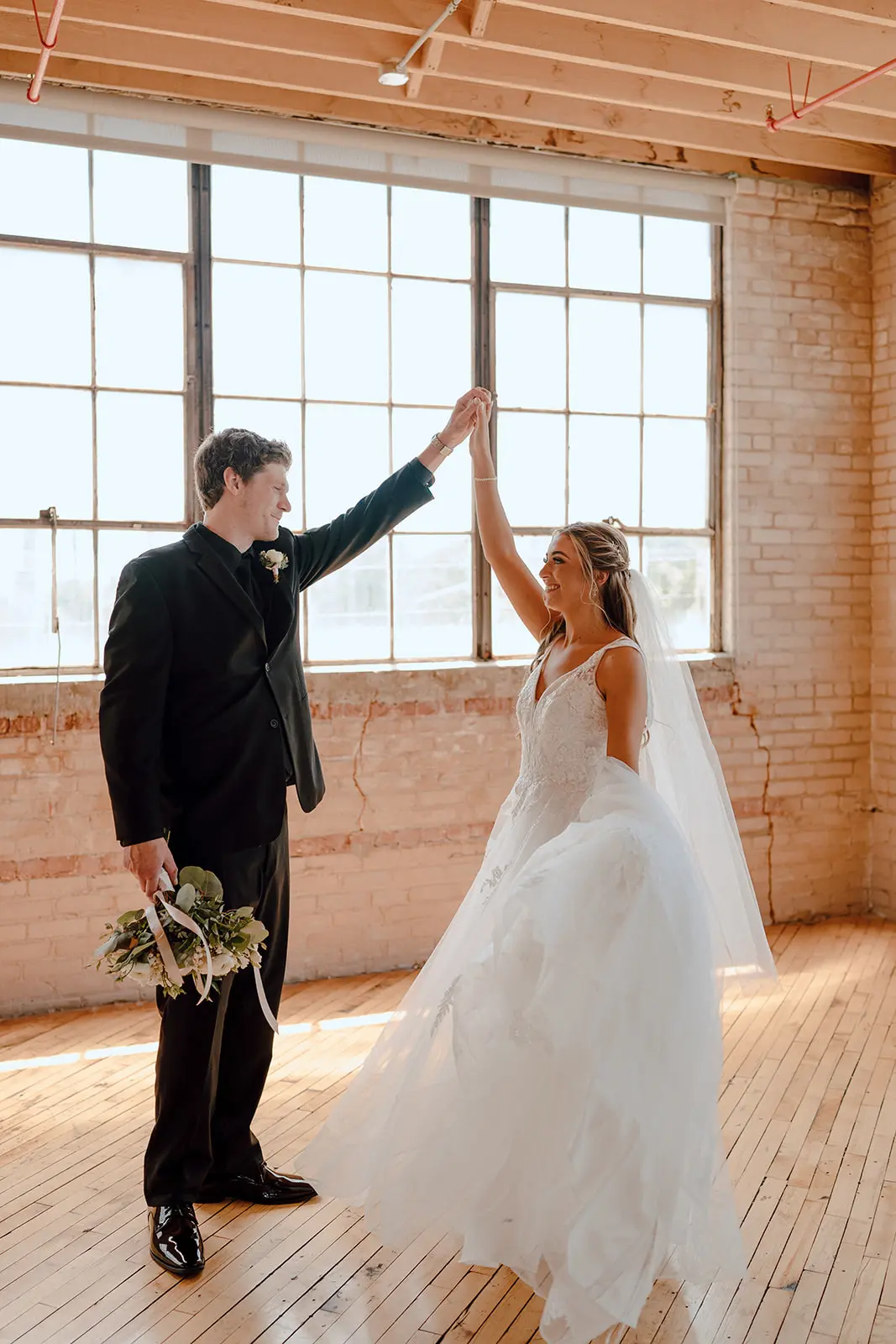 Bride Wearing Floral Ethereal Tulle Wedding Dress Called Lettie By Rebecca Ingram Holding Hand With Groom In The Air