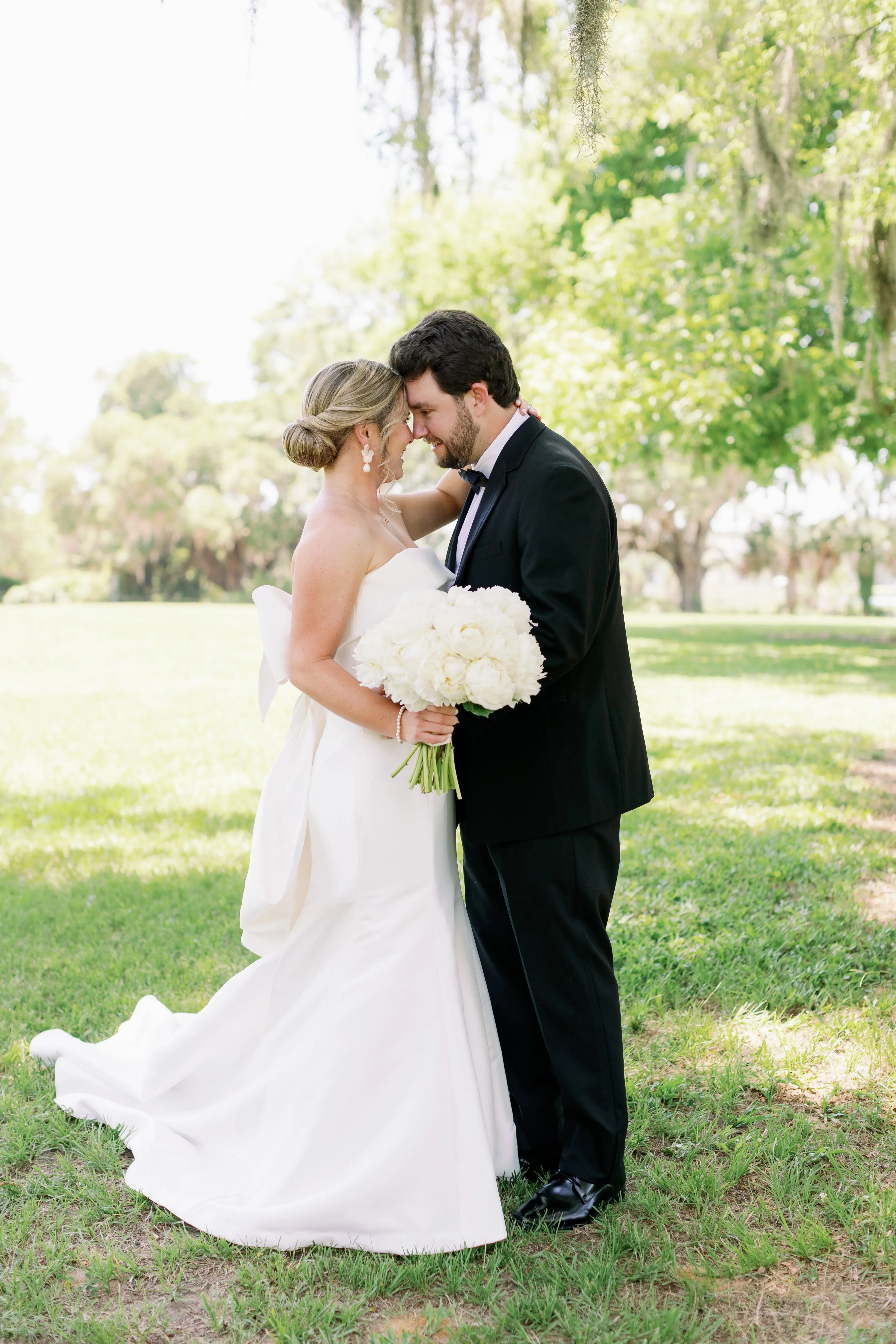 Bride with groom wearing strapless elegant mermaid wedding dress outdoors holding flower bouquet.