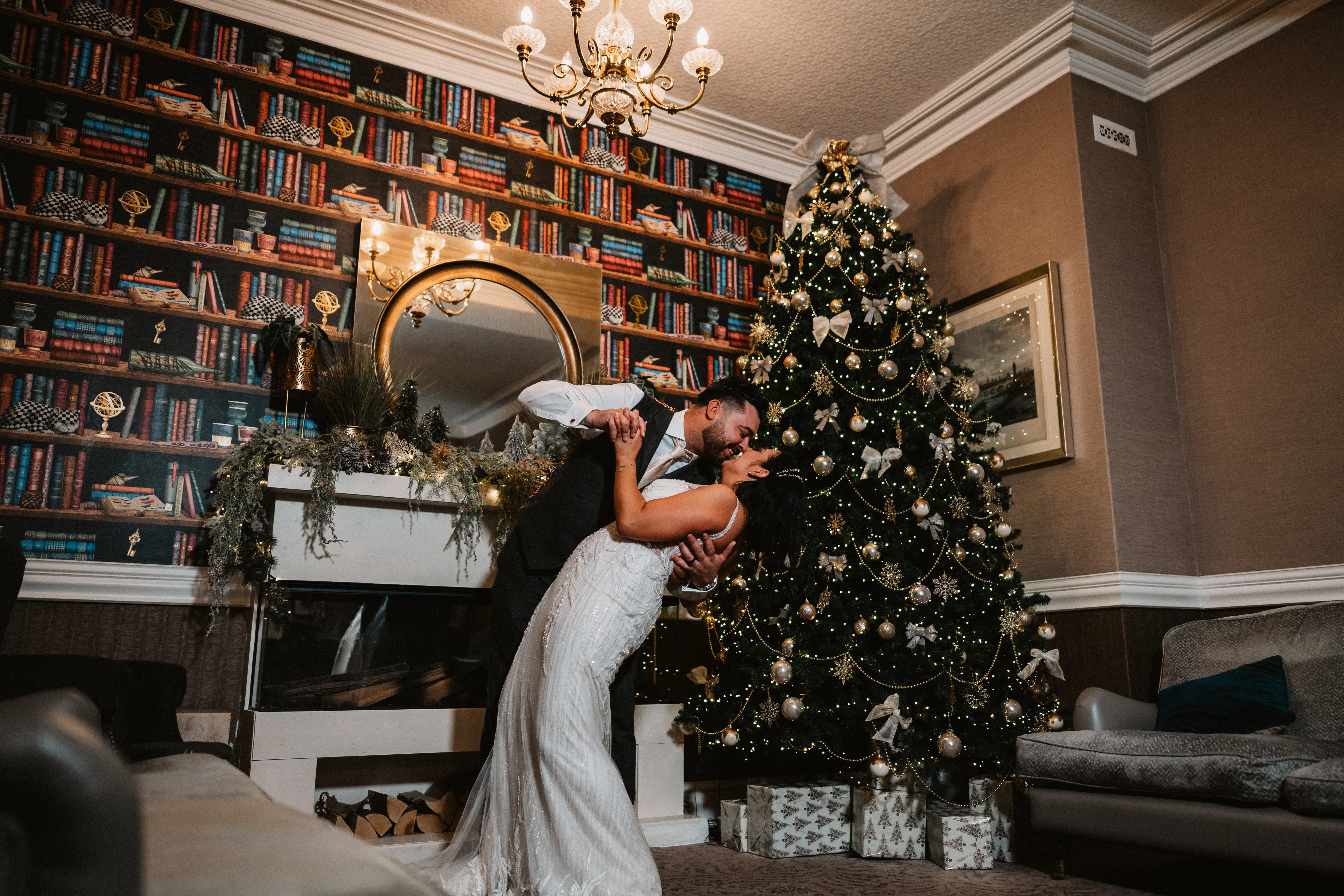 Bride Wearing Art Deco Wedding Dress Called Luella By Sottero And Midgley Kissing Groom Next To A Christmas Tree