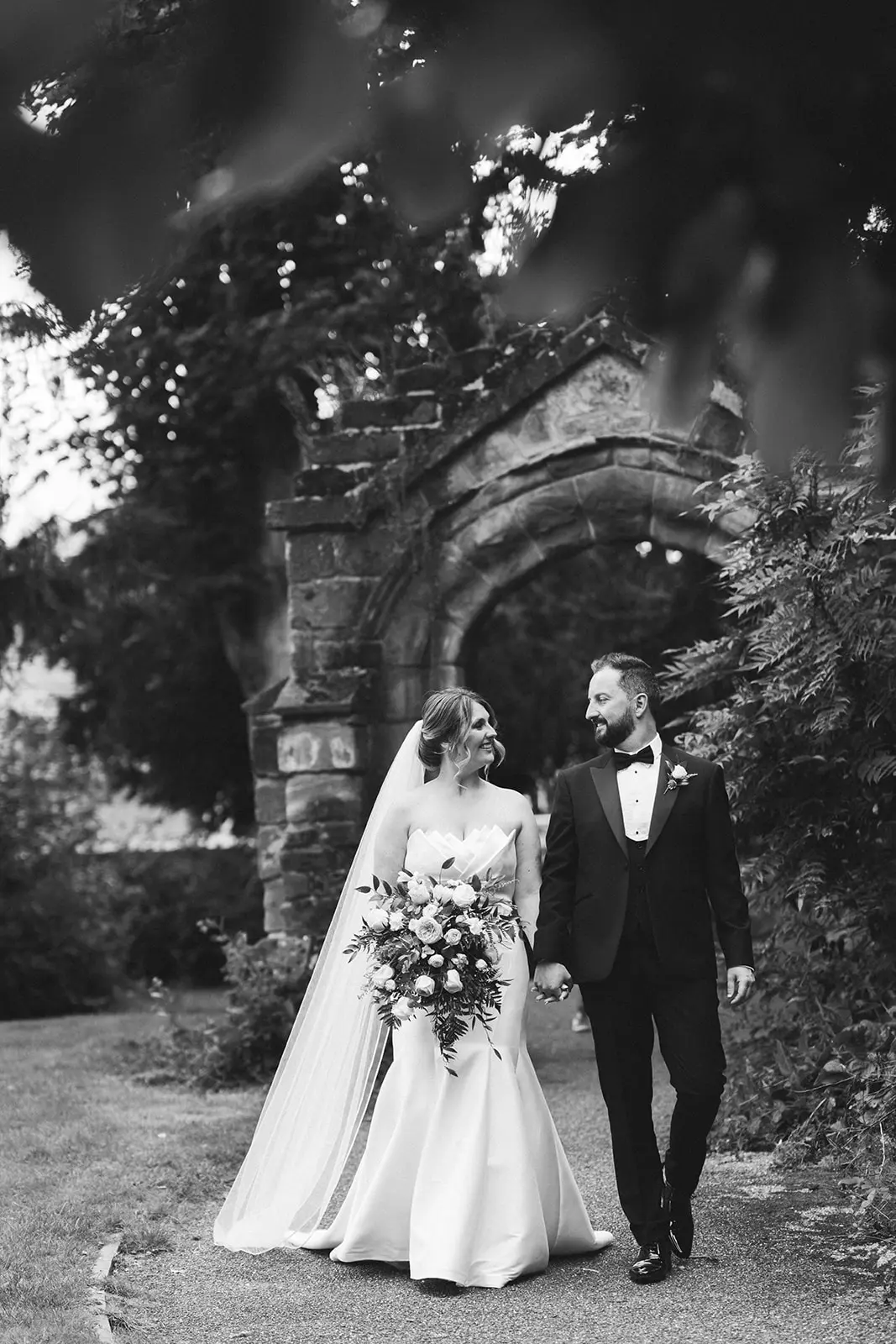 Bride Wearing Modern Wedding Dress Called Marilyn By Sottero And Midgley Walking With Groom In A Garden