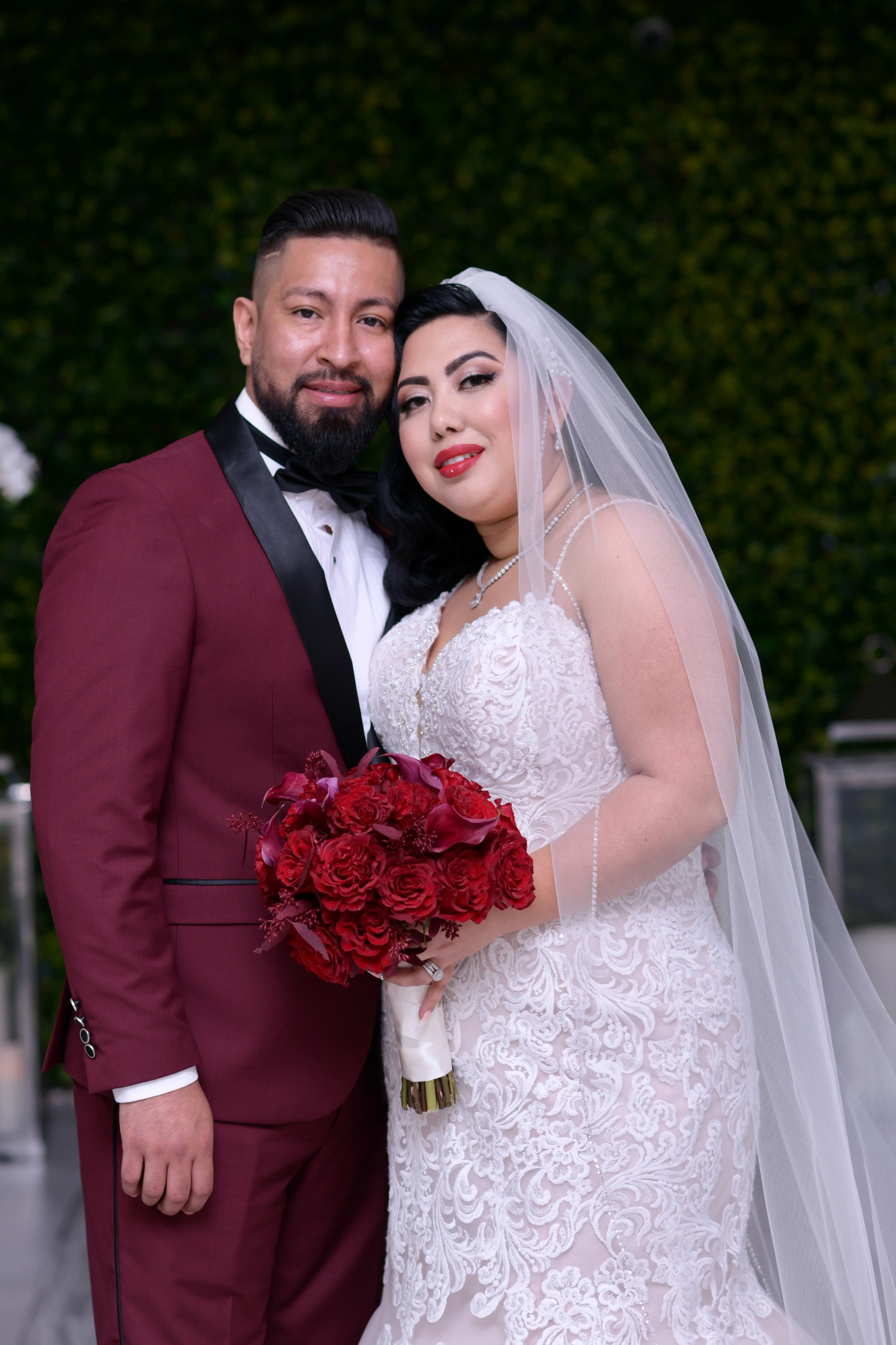 Bride wearing wedding dress called Alistaire Lynette holding a dark red bouquet standing with her groom.