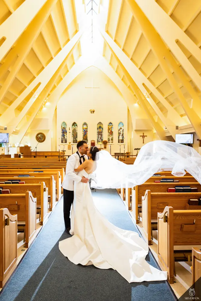 Bride And Groom Share Kiss In Chapel. Bride Wearing Unique Strapless Wedding Gown With Statement Bow Called Mitchell By Maggie Sottero