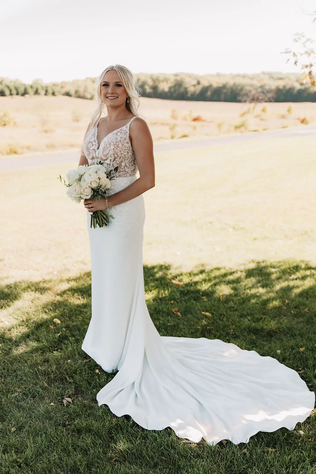 Bride wearing wedding dress called Carmen holding ivory bouquet standing in the shade.