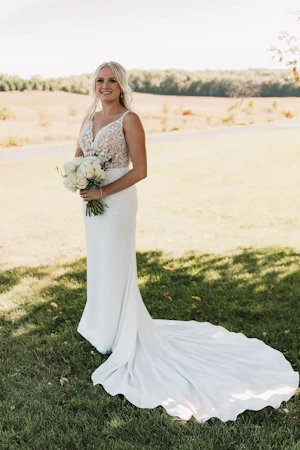 Bride wearing wedding dress called Carmen holding ivory bouquet standing in the shade.