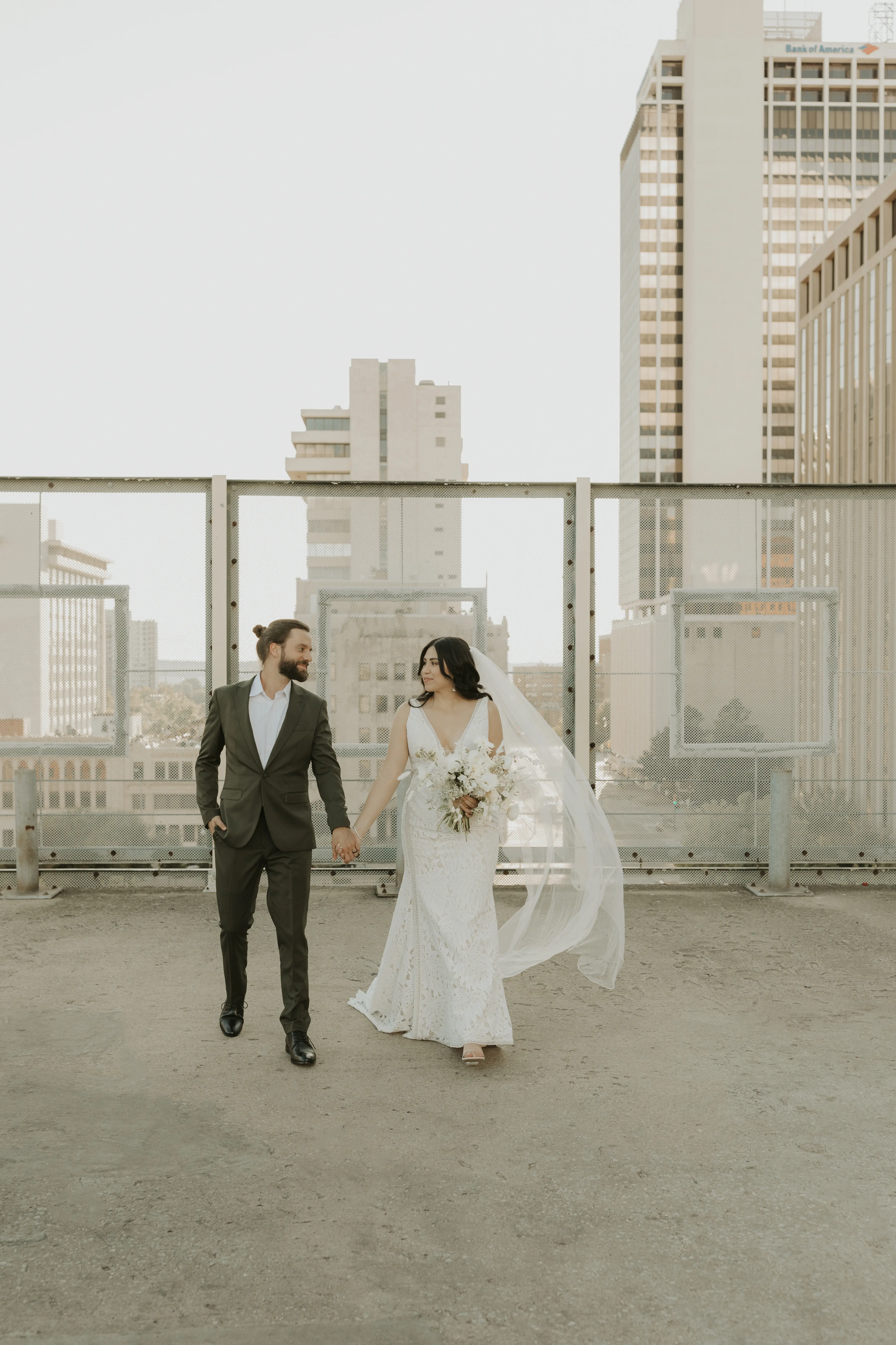 Bride and groom holding hands looking at each other on a roof top in the city.