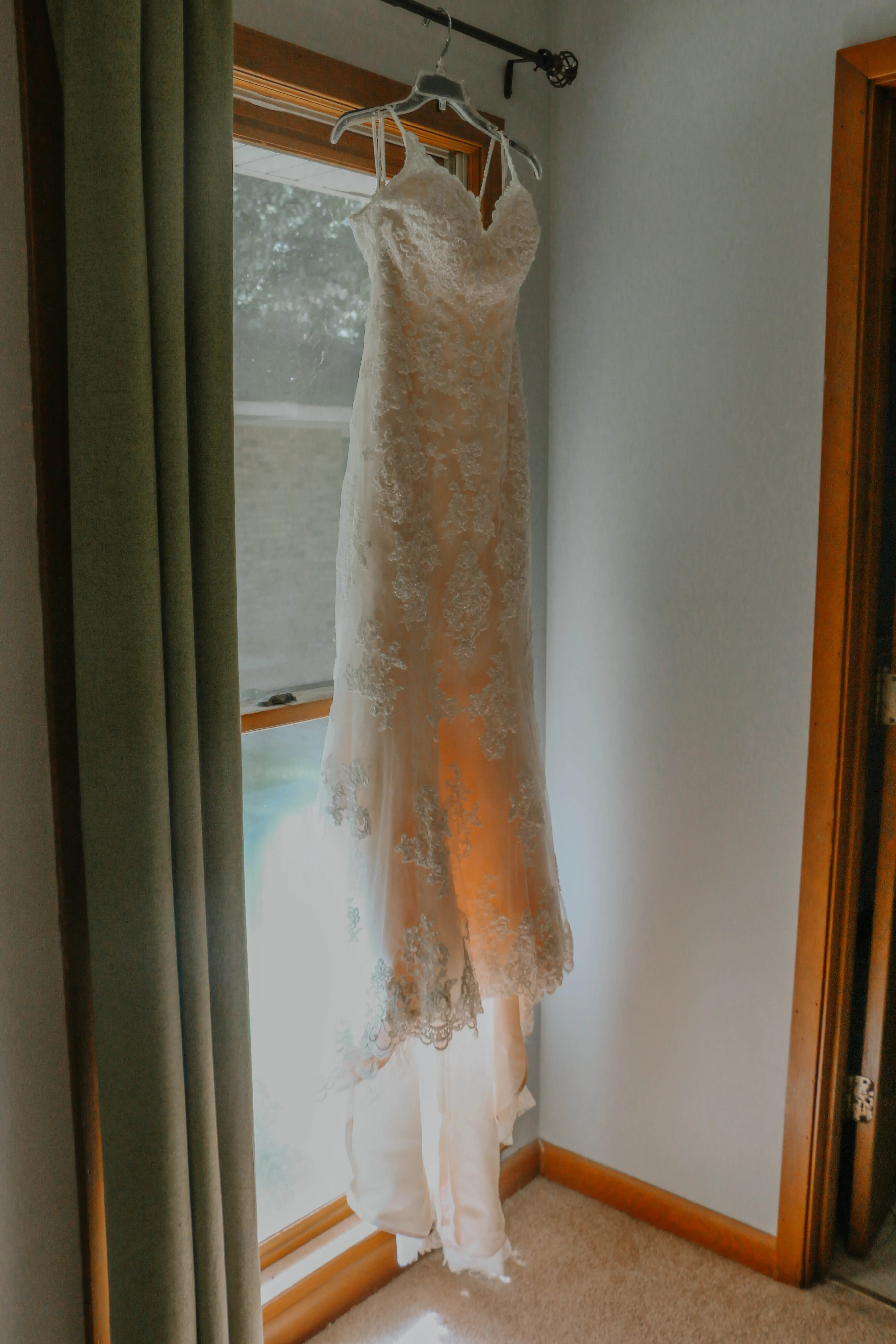 lace wedding dress called Drew hanging by the window.