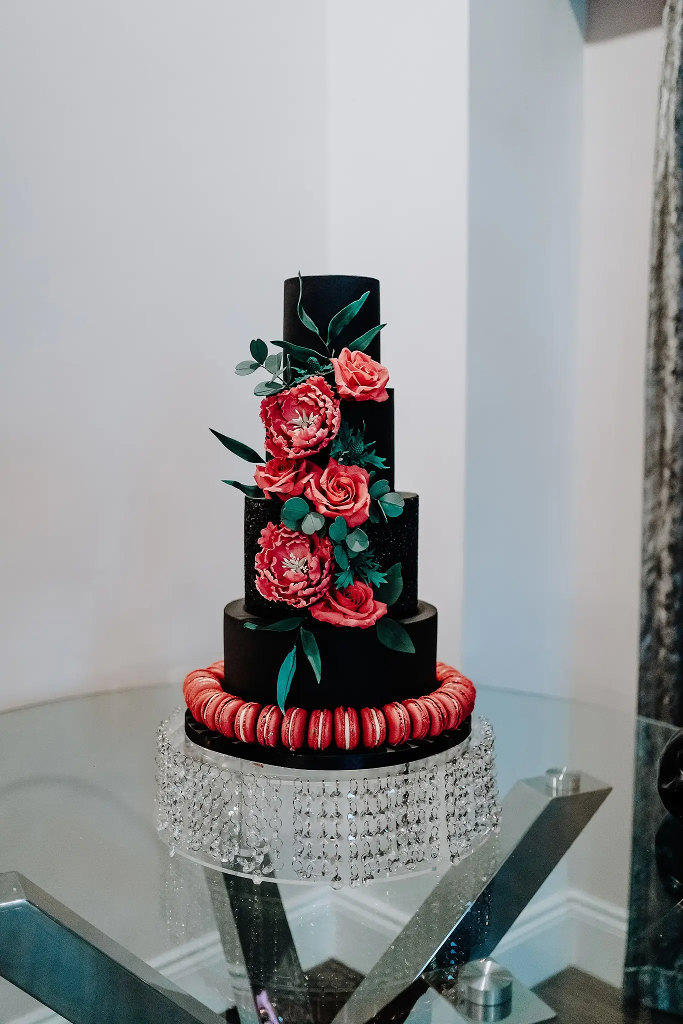 A Black Wedding Cake With Red Florals And Macaroons