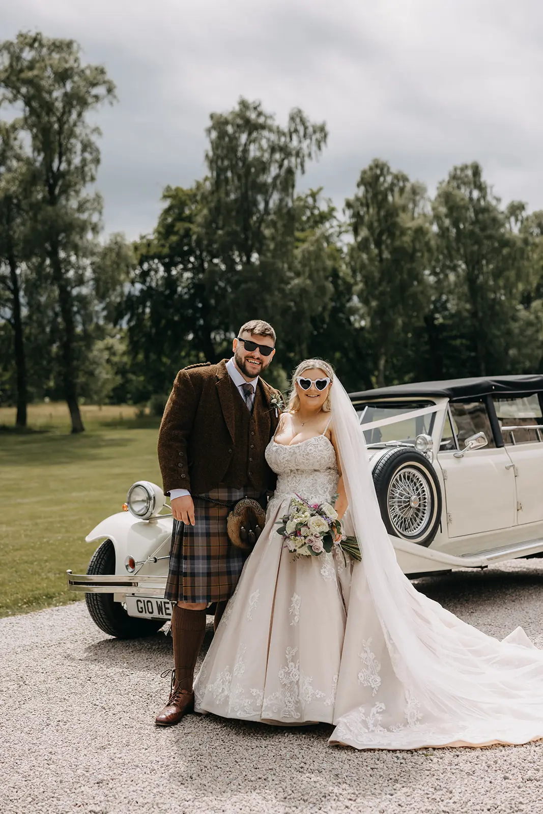 Bride wearing Norvinia by Sottero and Midgley wearing sunglasses with her husband outside of a car