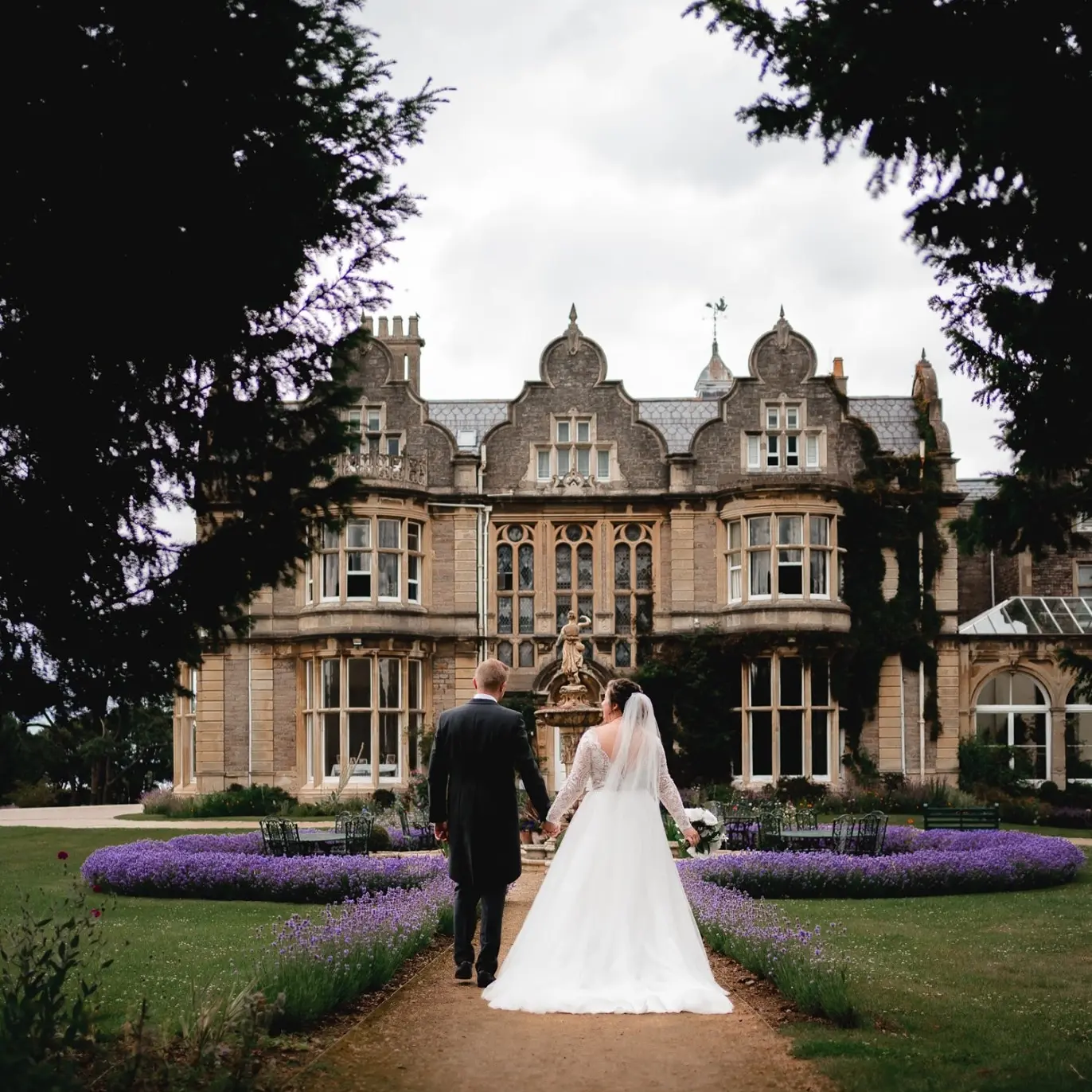 Bride Holding Grooms Hand From Back in Front of Castle Wearing Bridal Dress Called Mallory Dawn by Maggie Sottero