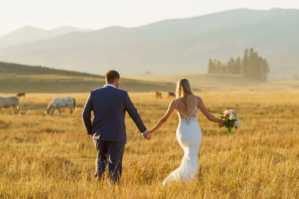 Bride wearing Dionne wedding dress by Rebecca Ingram walking through a field with her husband