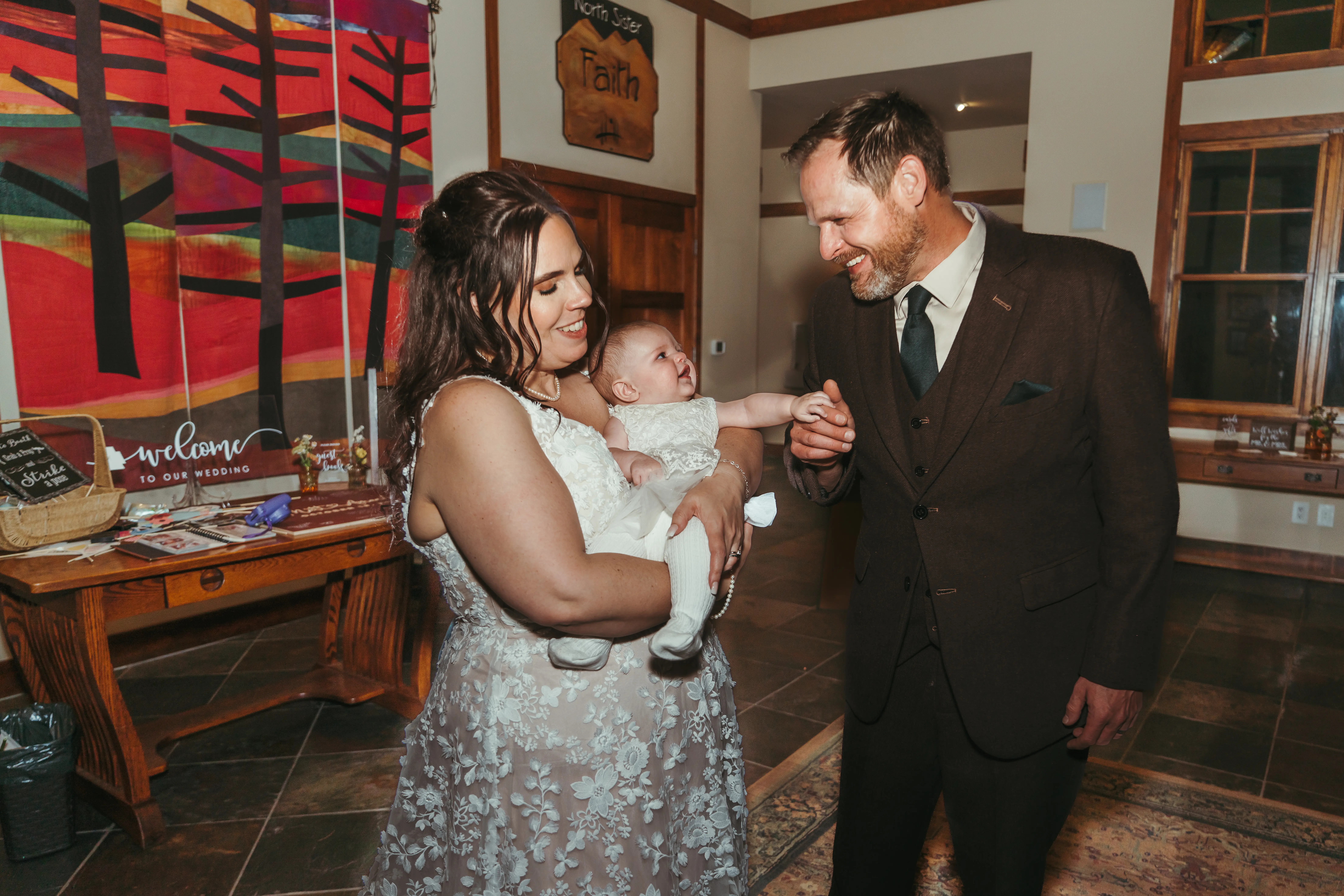Bride Wearing Lace Wedding Dress Called Ladonna By Maggie Sottero Holding Her Baby With Groom