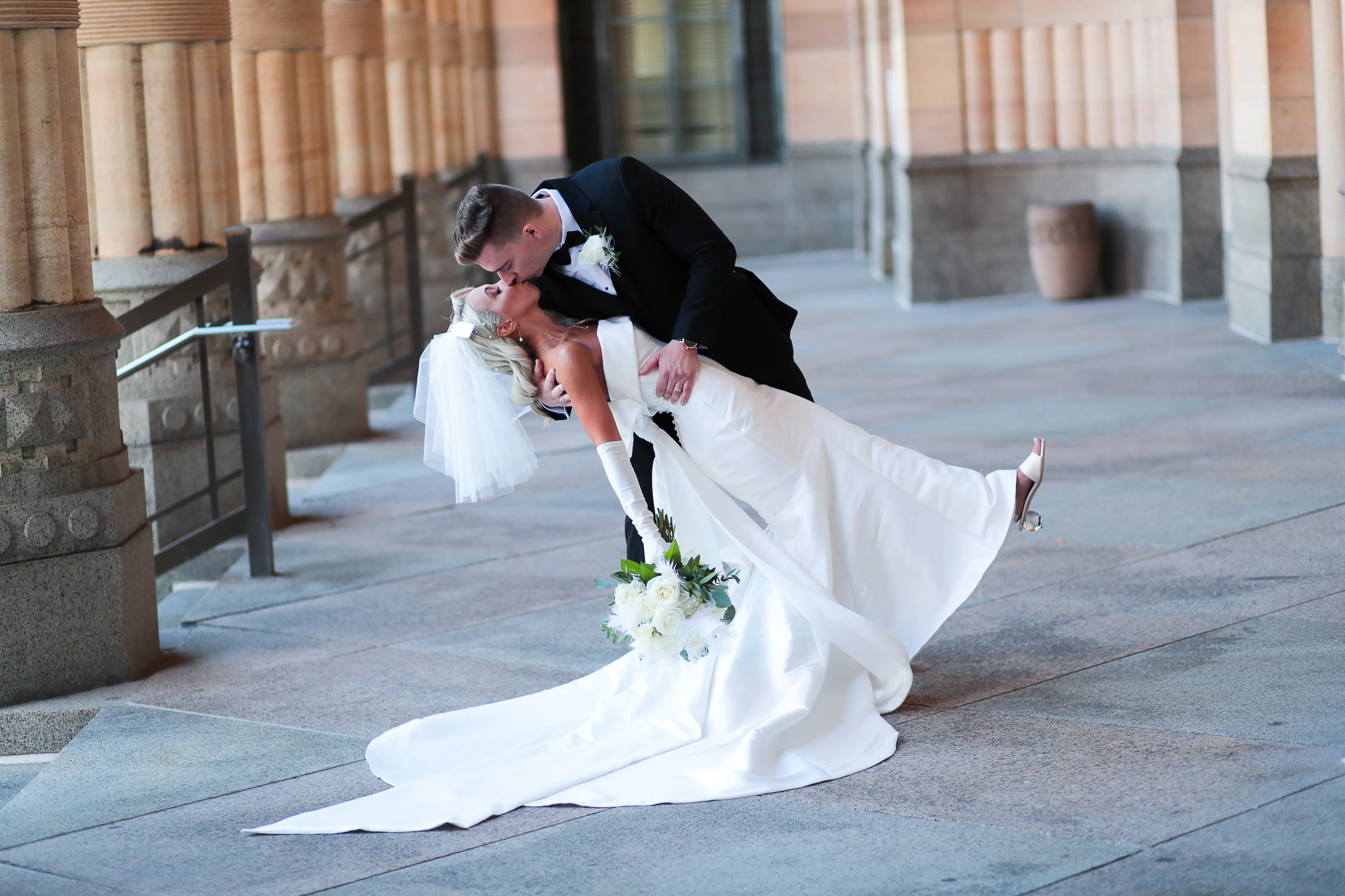 Bride In 90's Inspired Wedding Dress Called Mitchell By Maggie Sottero with Groom, Bridal Gloves, And Wedding Veil