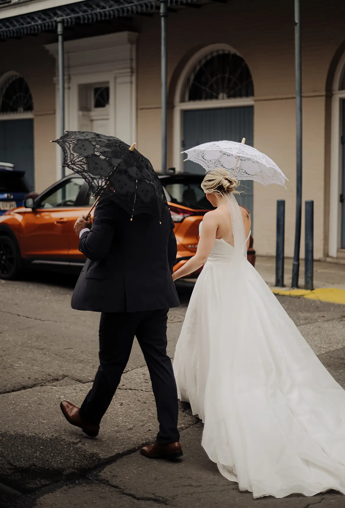 Bride Wearing Modern Princess Wedding Dress Called Aubrielle By Maggie Sottero Walking With Groom Each Holding Umbrellas