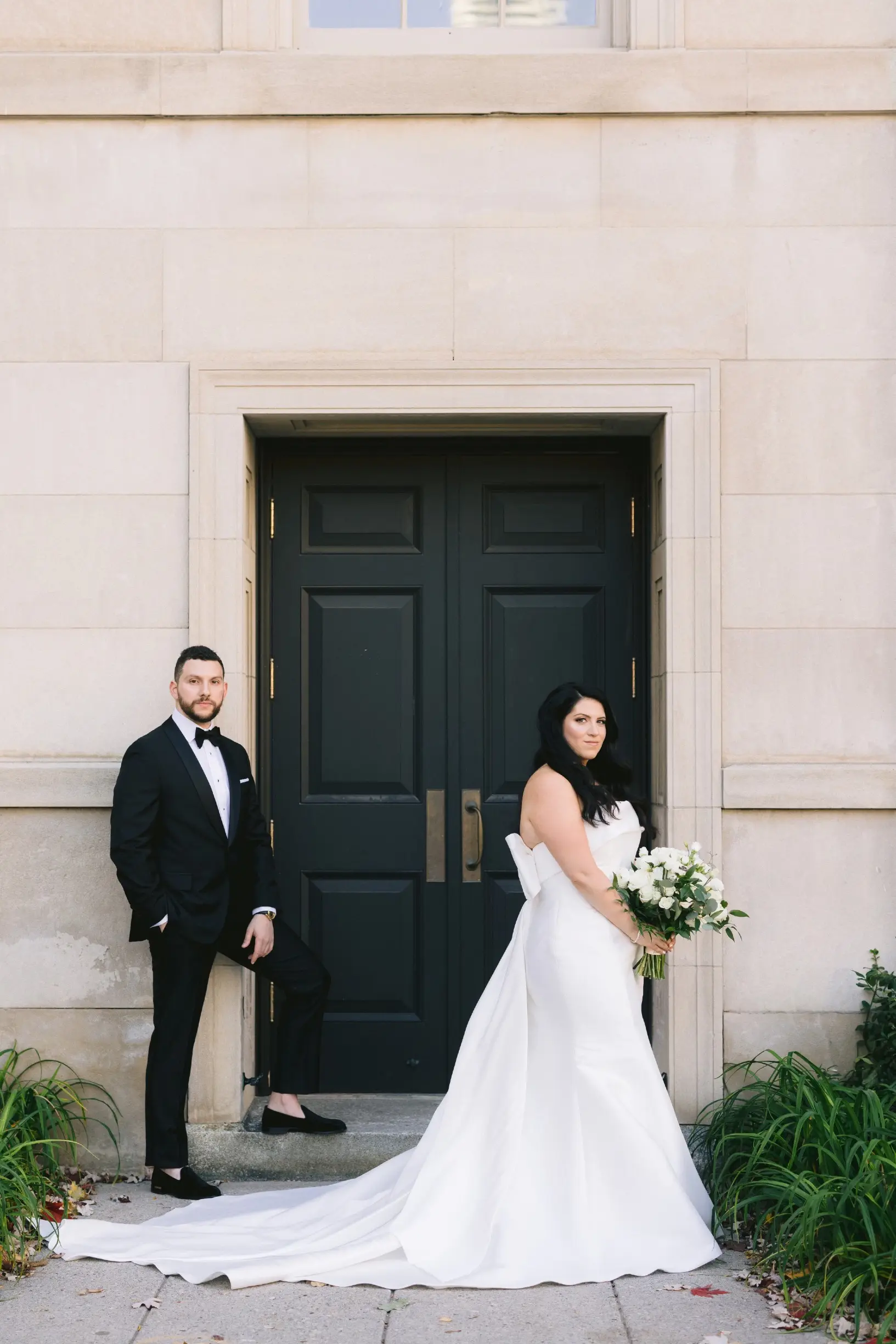 Bride with groom wearing strapless satin mermaid wedding dress with big bow on the back.
