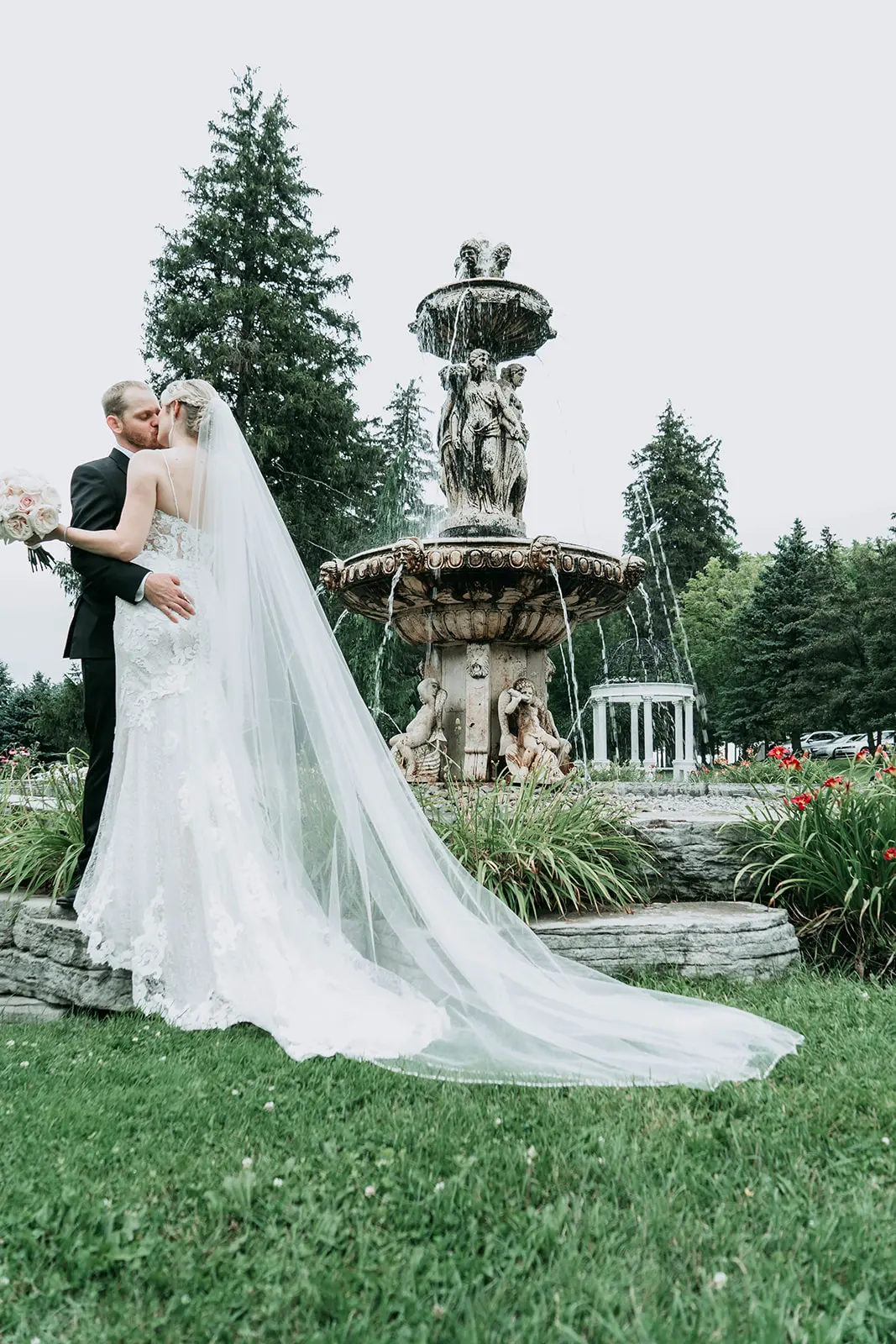 Newlyweds kissing by a large water fountain.