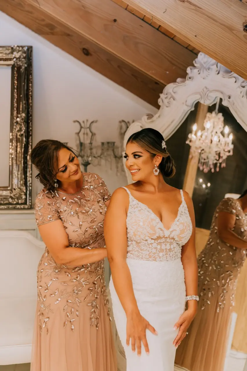 Mother of bride smiling at her daughter as she fastens her wedding dress called Carmen.