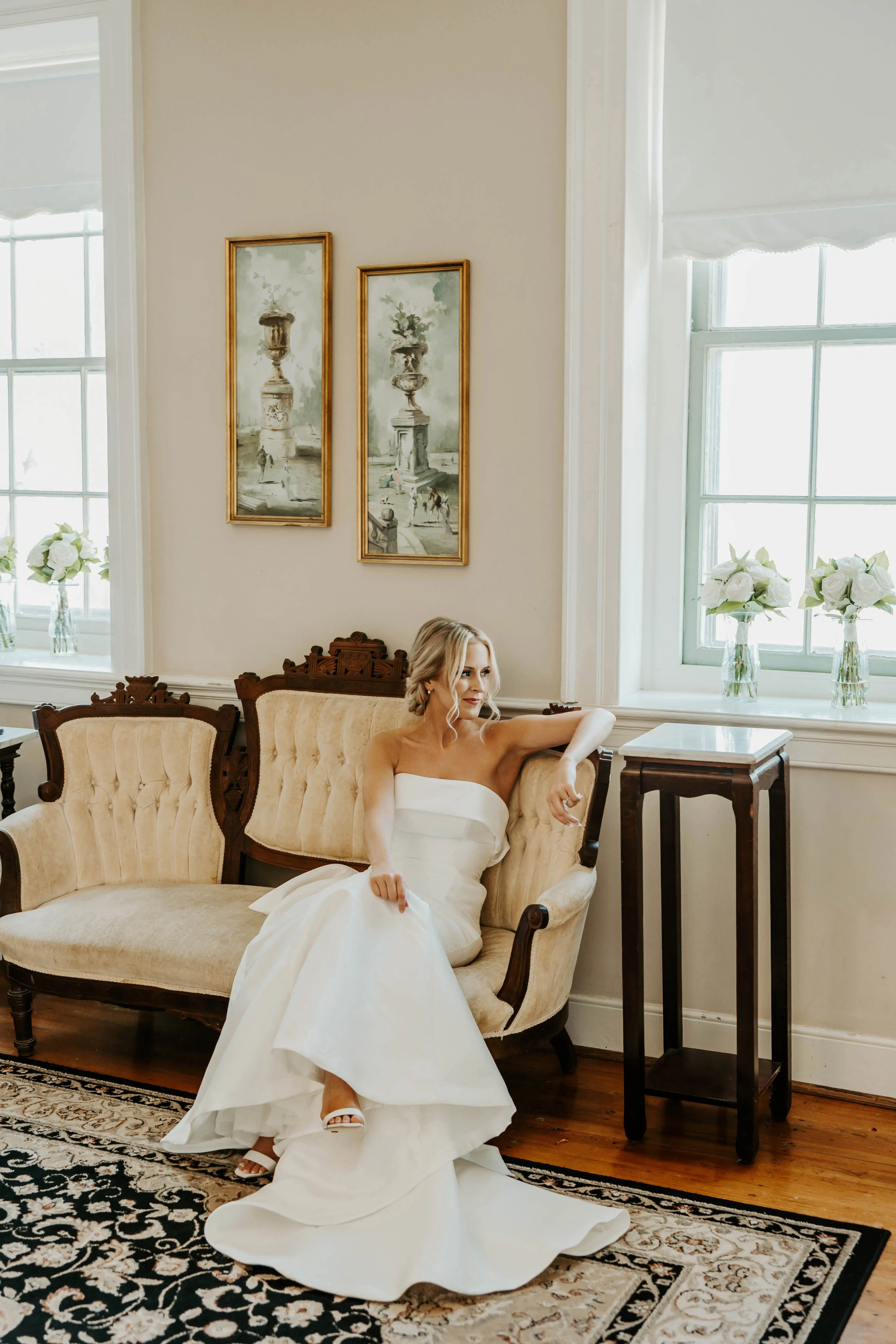 Bride Sitting On A Couch In A White Strapless Wedding Dress Named Mitchell By Maggie Sottero