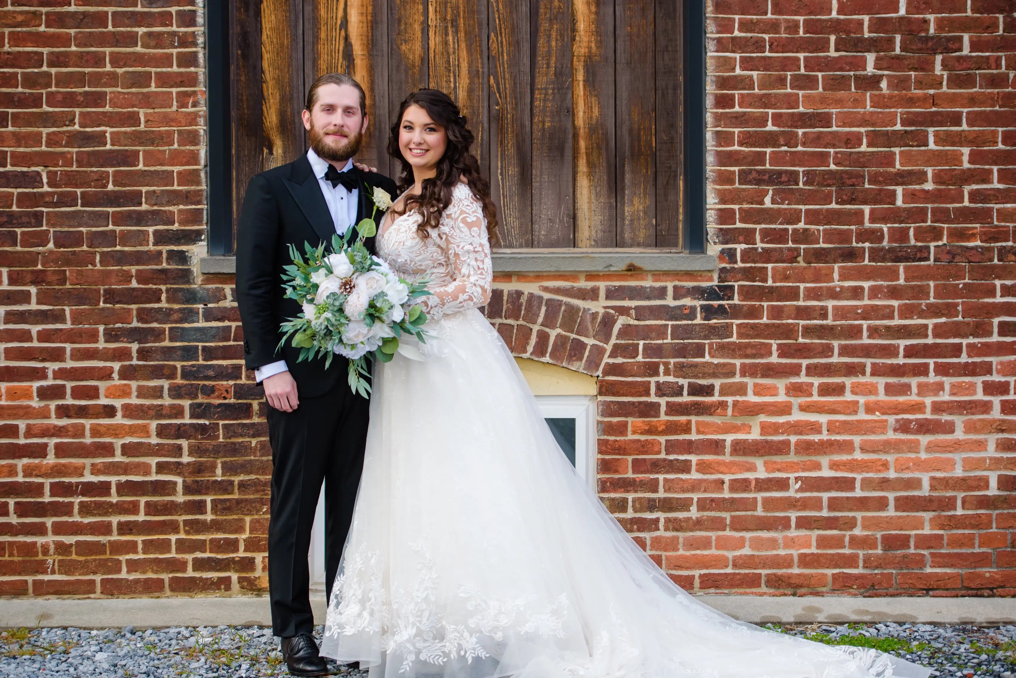 Bride And Groom Standing Together. Bride Wearing Lace Long Sleeve Wedding Dress Called Zander By Sottero And Midgley